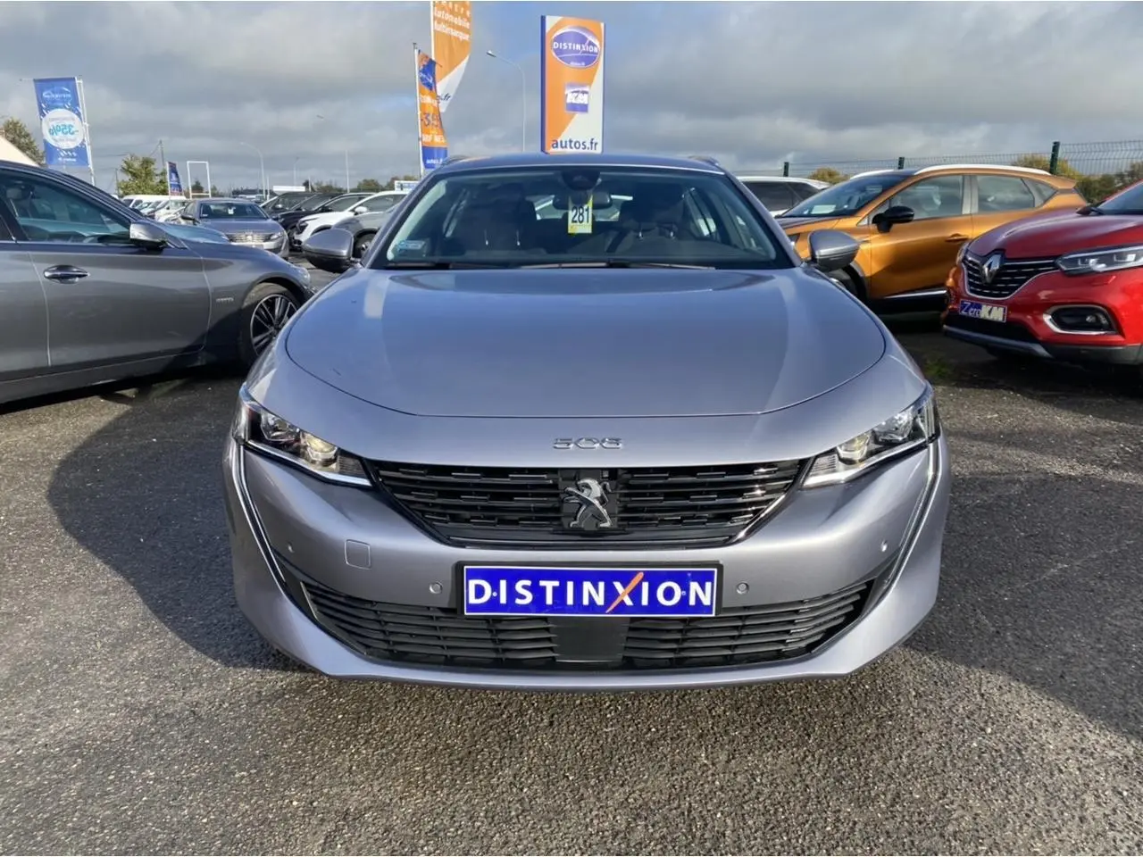 Vue frontale d'une Peugeot 508 SW gris Artense avec calandre noire et logo lion au centre, stationnée en extérieur.