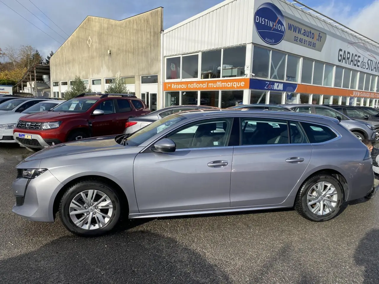 Profil droit d'une Peugeot 508 SW gris Artense 2021 stationnée devant un garage multimarque.