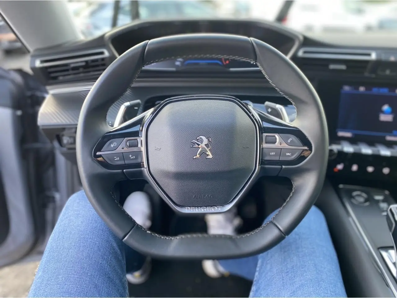 Vue rapprochée du volant compact noir du Peugeot 508 SW 2021, avec tableau de bord numérique en arrière-plan flou.