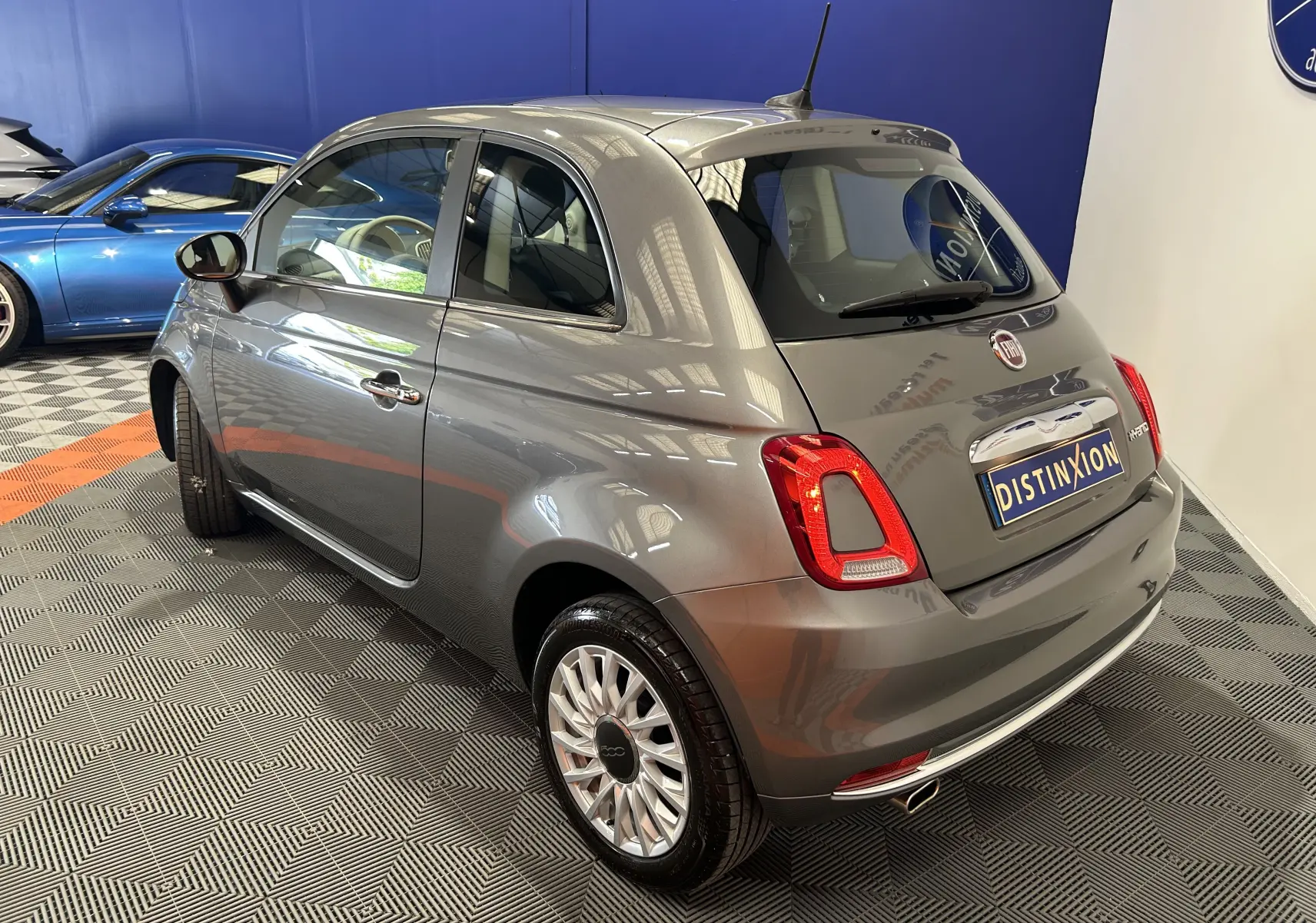 Vue 3/4 arrière droite d'une FIAT 500 gris métallisé avec toit panoramique, en intérieur showroom.