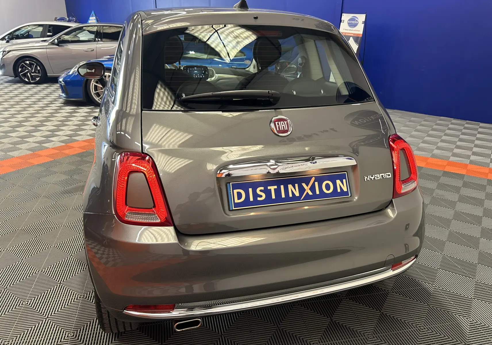 Vue arrière d'une FIAT 500 gris métallisé hybride avec toit panoramique dans un showroom.
