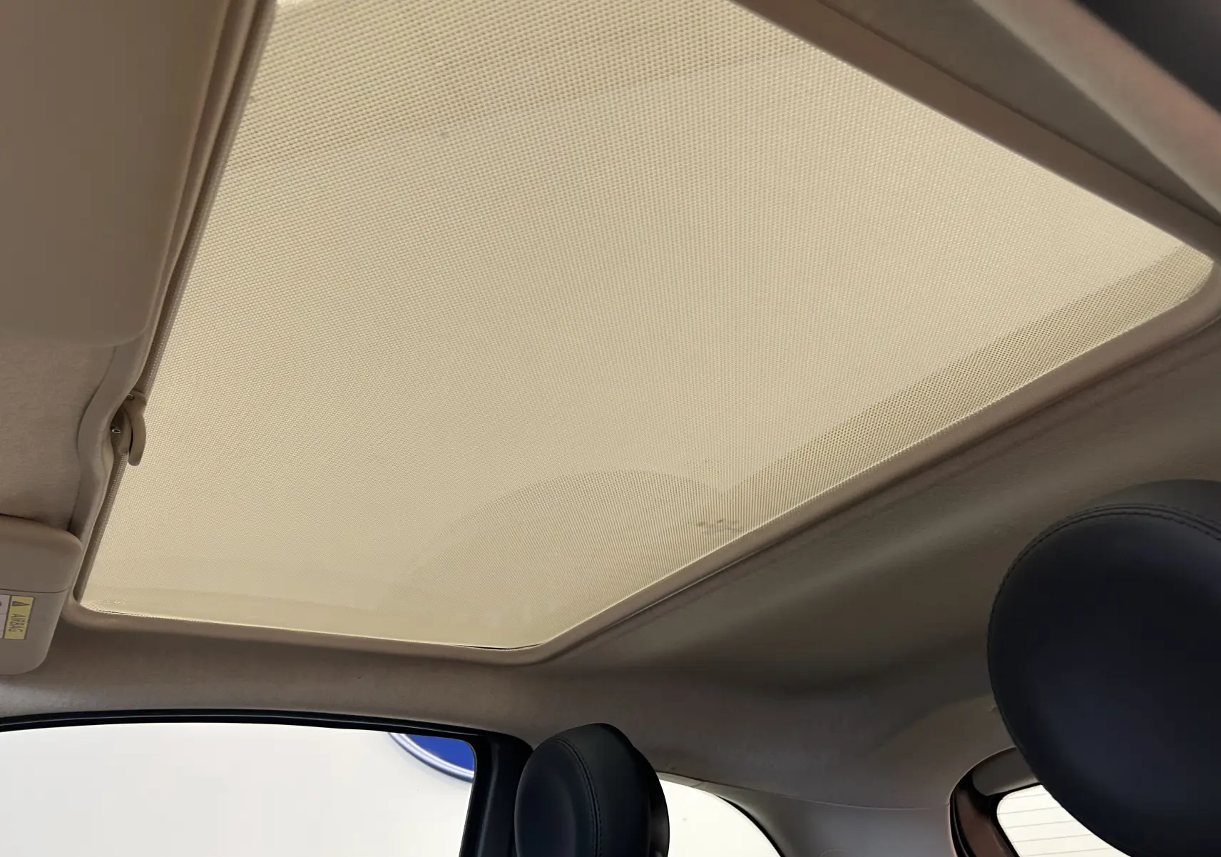 Vue intérieure du toit panoramique avec pare-soleil déployé et appuie-tête en cuir noir d'une Fiat 500 grise.