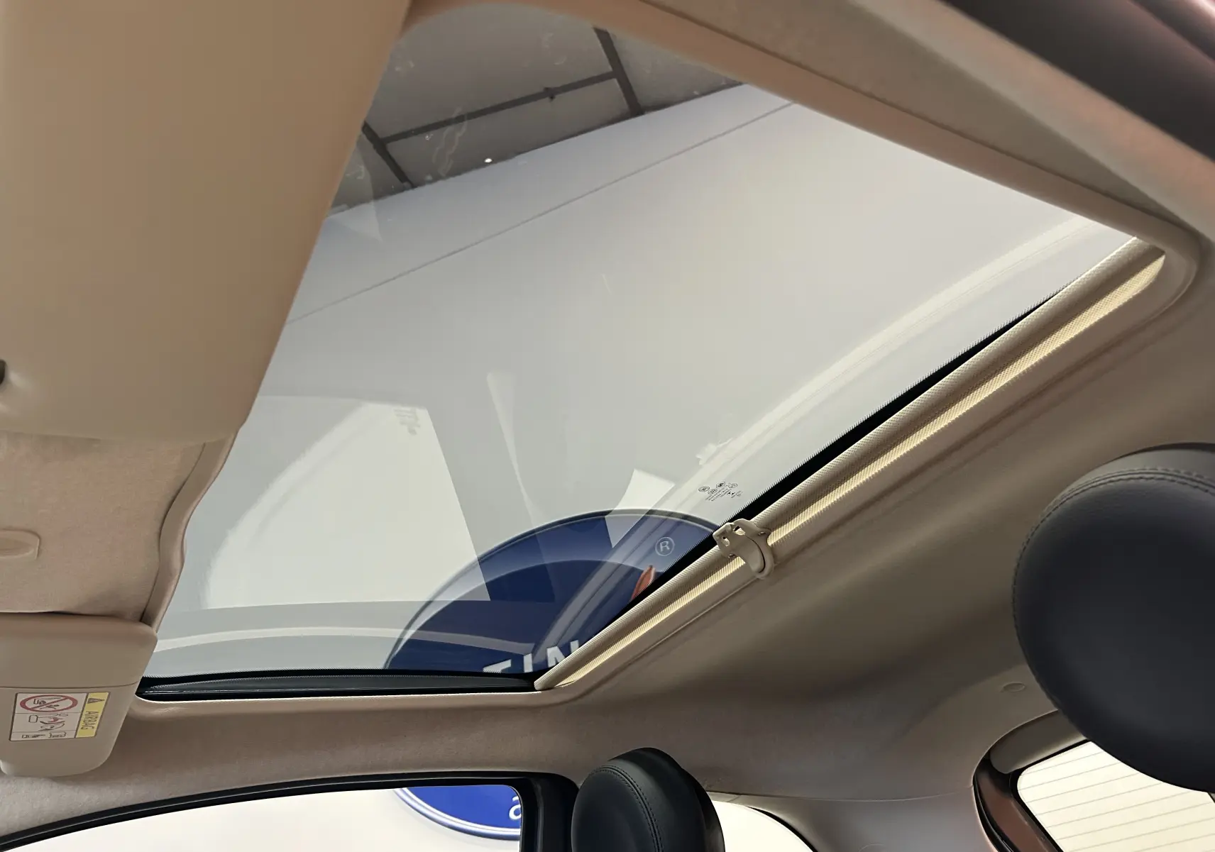 Toit panoramique ouvert vu de l'intérieur côté gauche d'une Fiat 500 gris clair avec sièges en cuir noir.