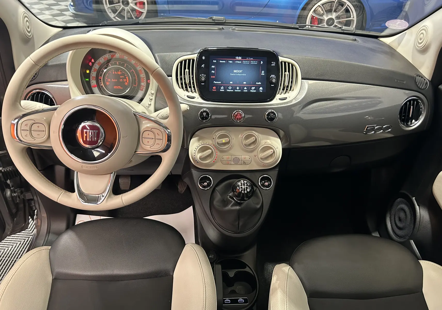 Vue intérieure frontale du tableau de bord beige et noir de la Fiat 500 avec volant clair et écran tactile central.