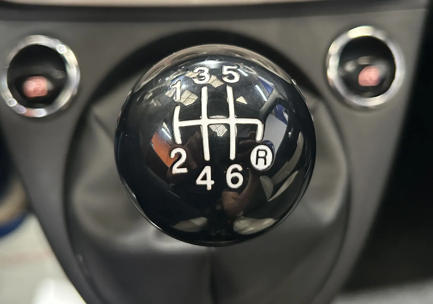 Gros plan sur le pommeau noir de la boîte manuelle 6 vitesses de la FIAT 500 hybride gris, avec marquages blancs.