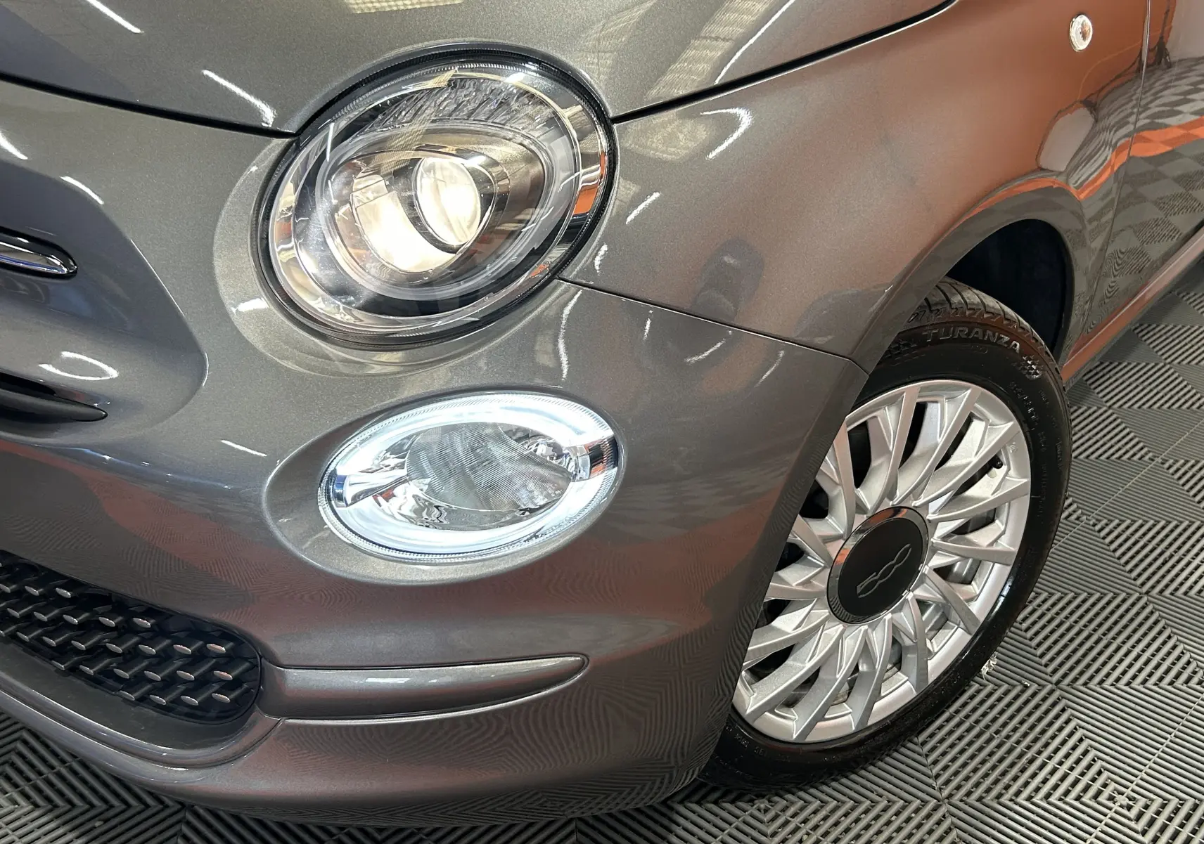 Gros plan sur l'avant droit gris métallisé d'une FIAT 500 avec phare rond et jante alliage élégante.