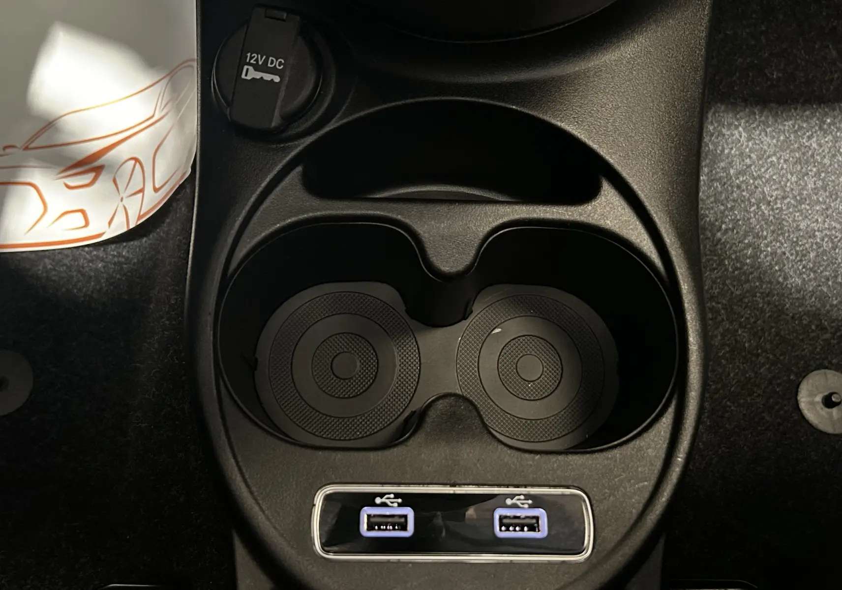 Vue plongeante sur la console centrale noire de la Fiat 500 avec porte-gobelets et deux ports USB éclairés.