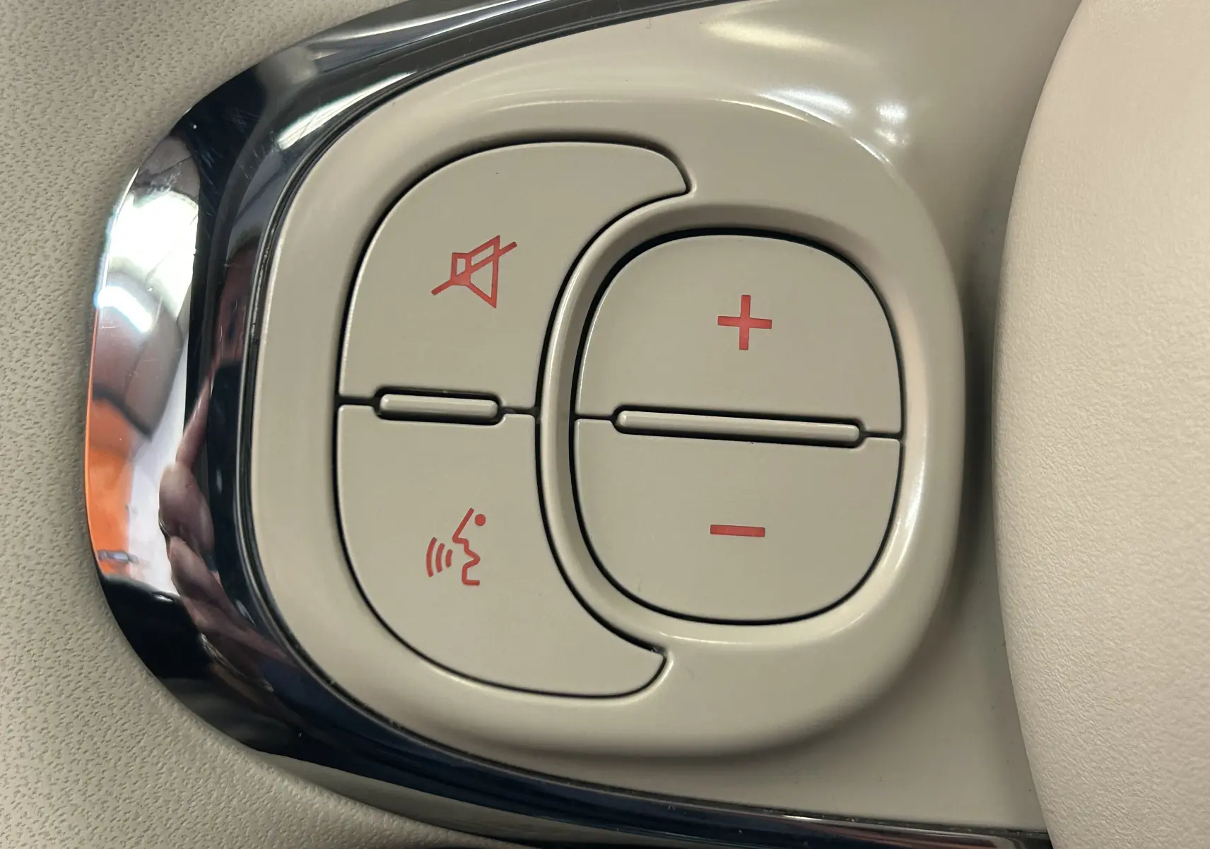 Gros plan sur les commandes de volume et de coupure du son en plastique beige avec cadre chromé dans une Fiat 500 gris clair.