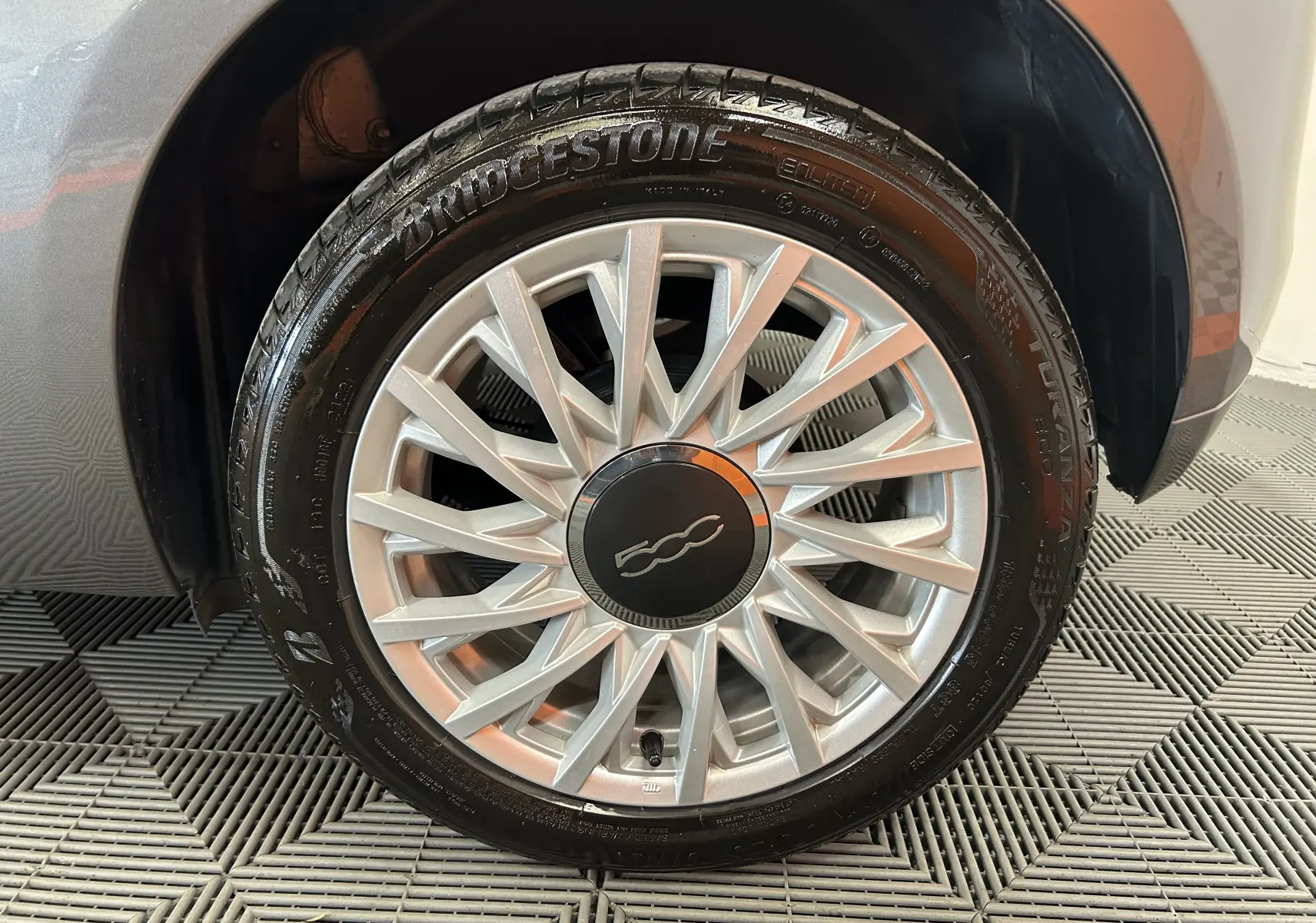 Gros plan sur la roue avant droite gris métallisé de la FIAT 500 70 Hybride BSG DolceVita avec jante argentée et logo 500.