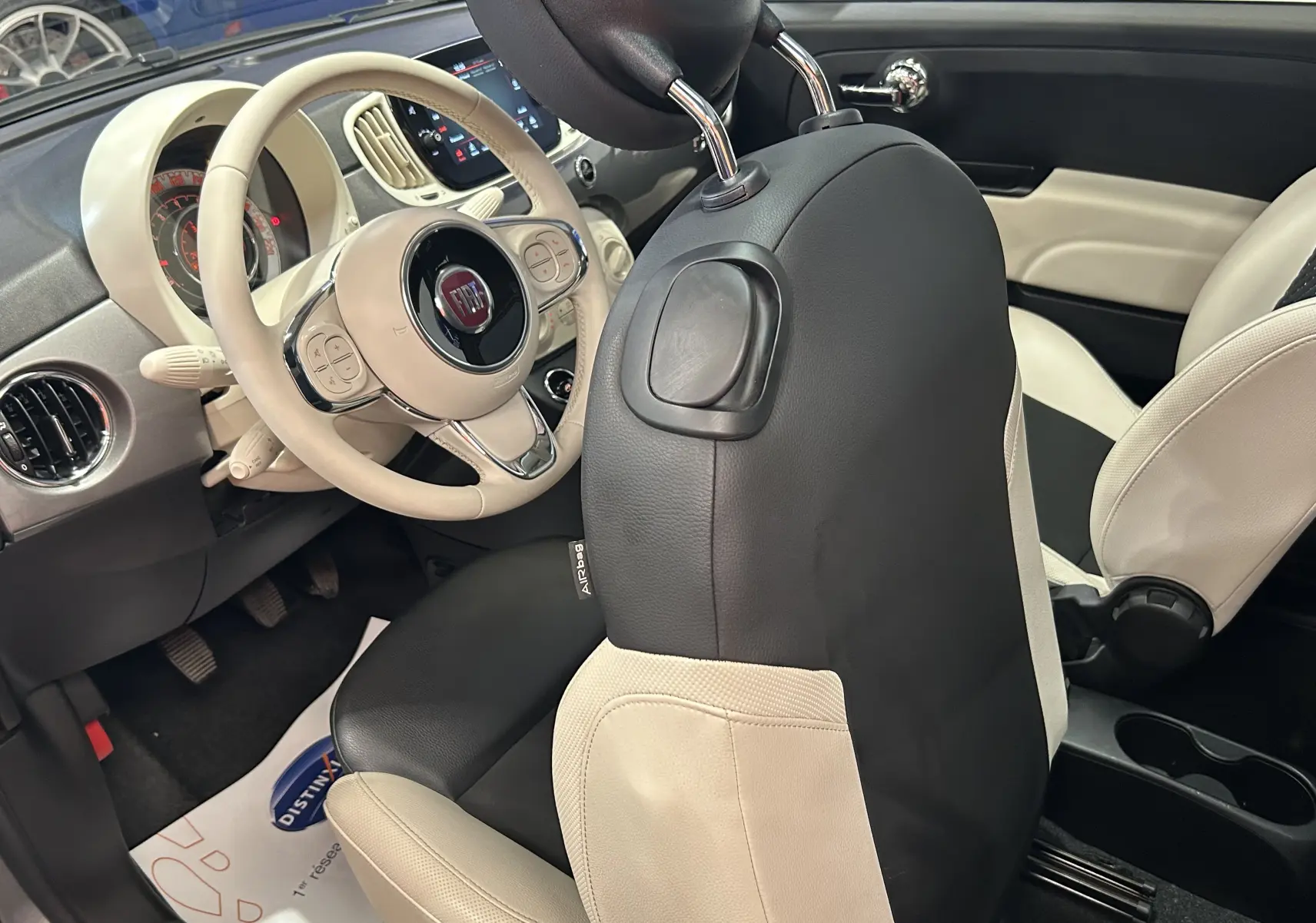 Intérieur de la Fiat 500 gris, vue côté conducteur, volant beige et sièges bi-color noir et blanc en cuir.