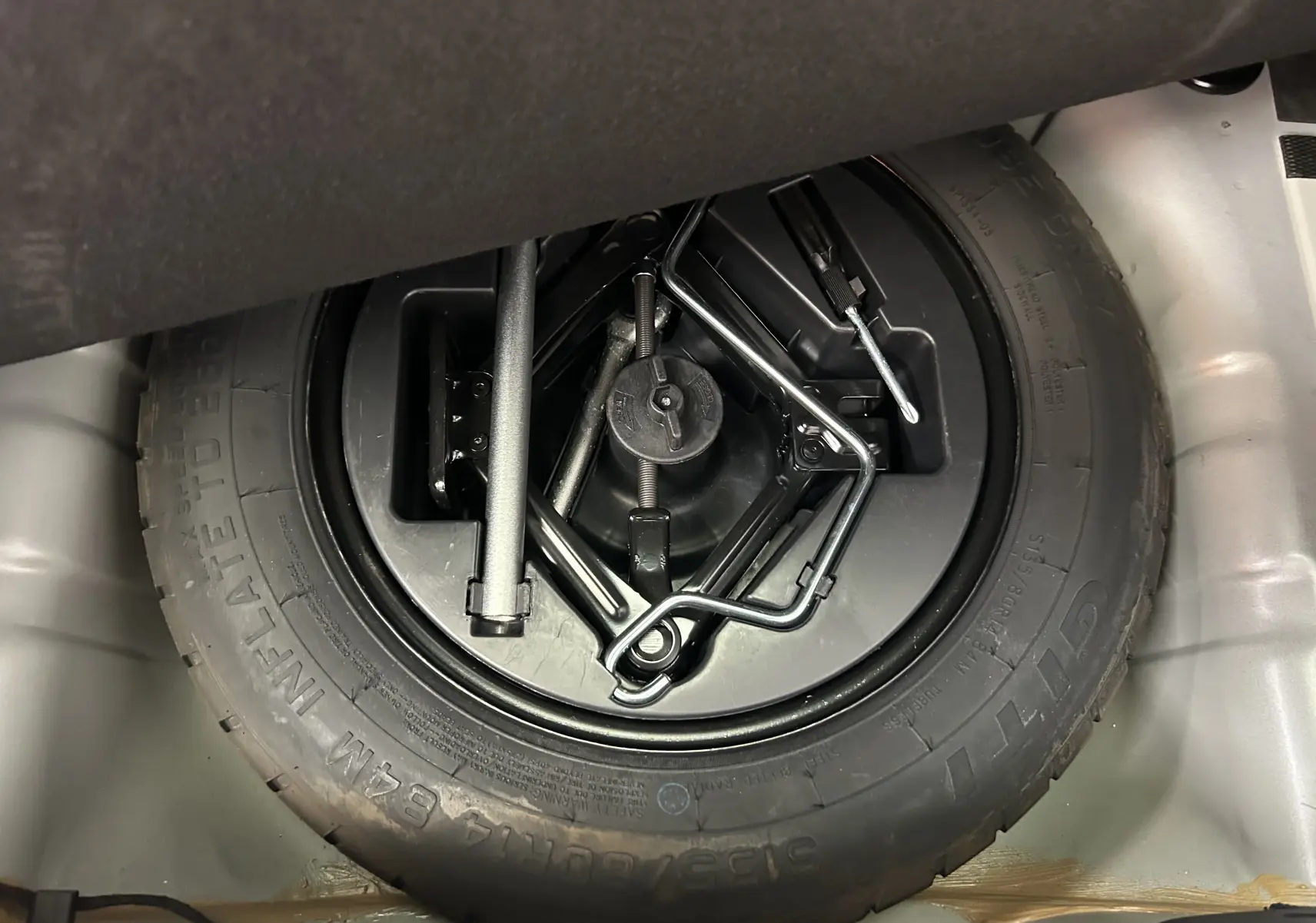 Gros plan sur la roue de secours et les outils de bord dans le coffre d'une FIAT 500 gris 70 Hybride BSG DolceVita 2022.