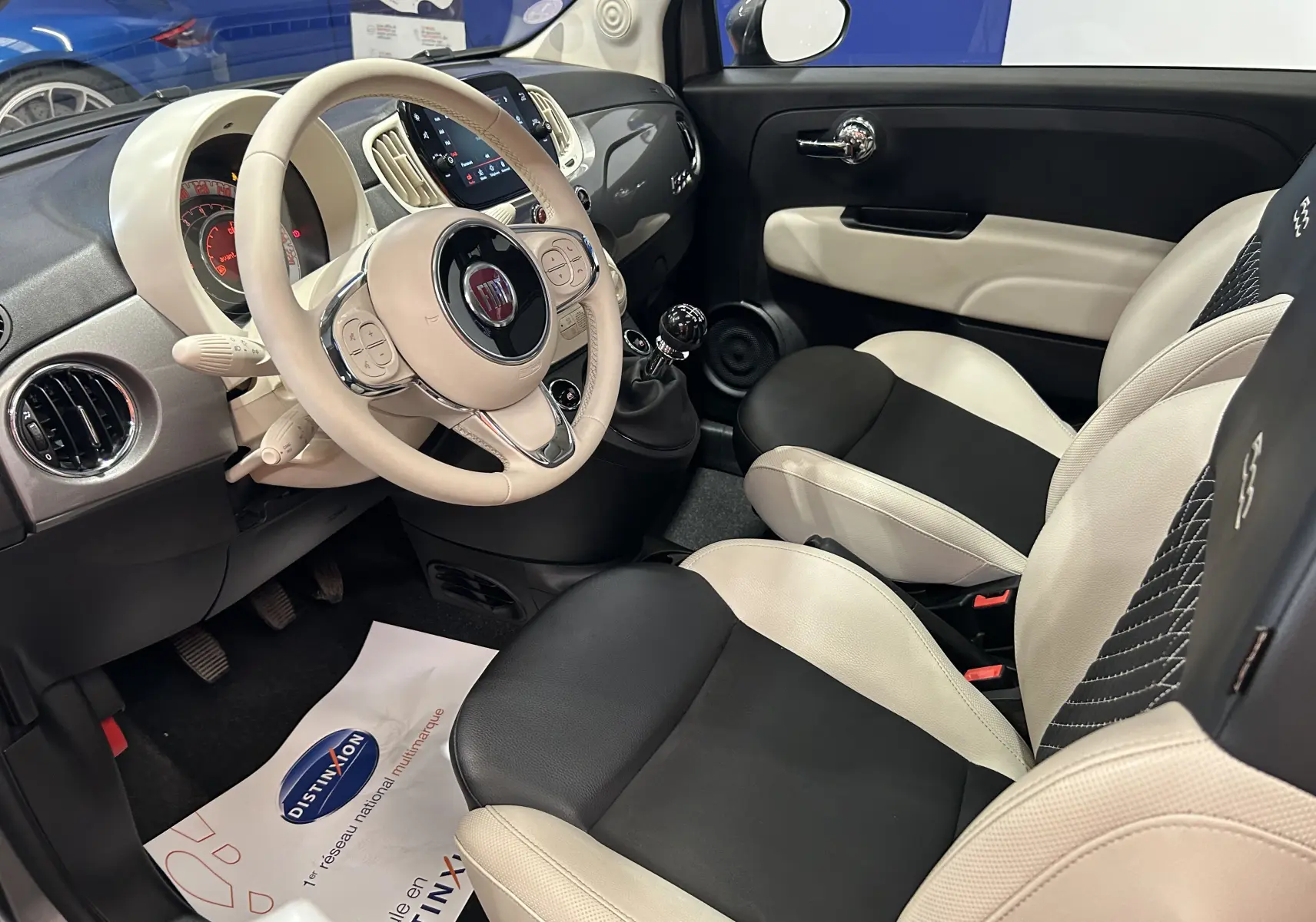 Intérieur de la Fiat 500 gris vue côté conducteur, avec volant beige, sièges bicolores noir et beige et tableau de bord moderne.