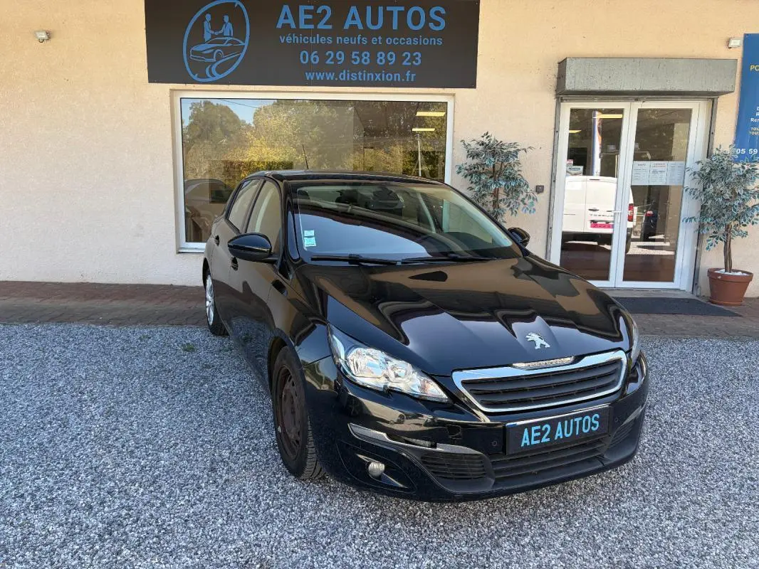 Peugeot 308 Active noire vue en 3/4 avant droit, stationnée devant un garage AE2 Autos sur gravier.