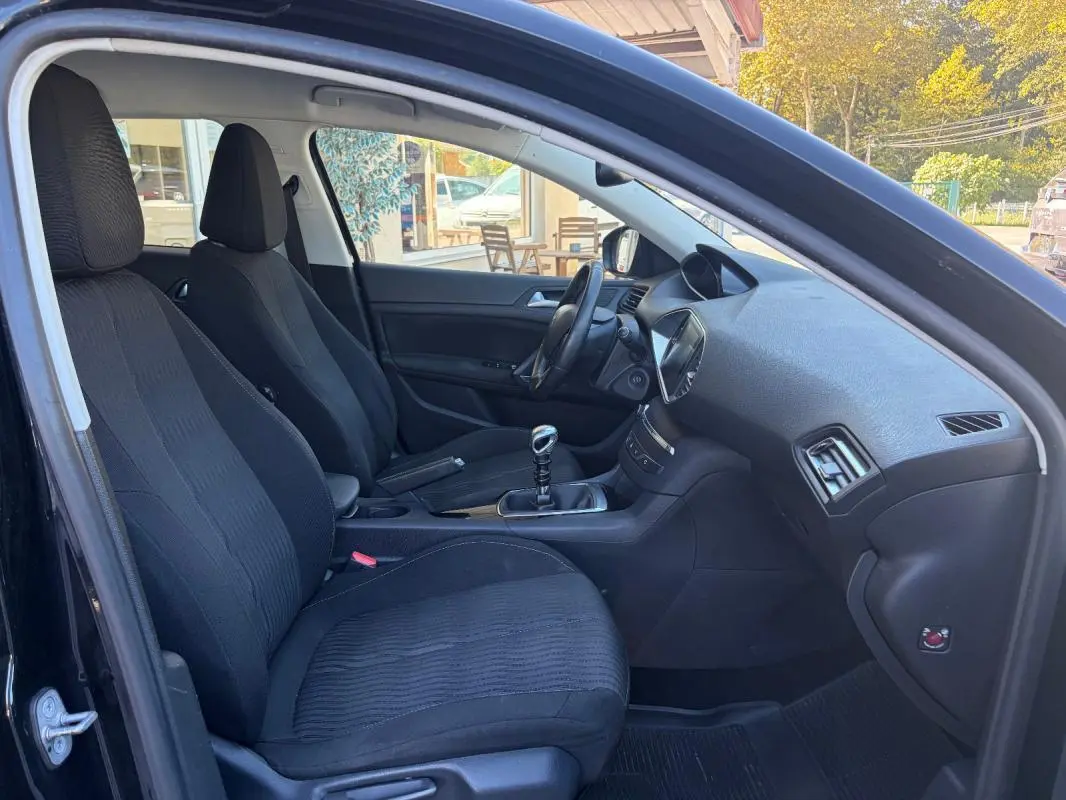 Vue intérieure côté conducteur de la Peugeot 308 noire de 2014, montrant les sièges et la boîte manuelle.