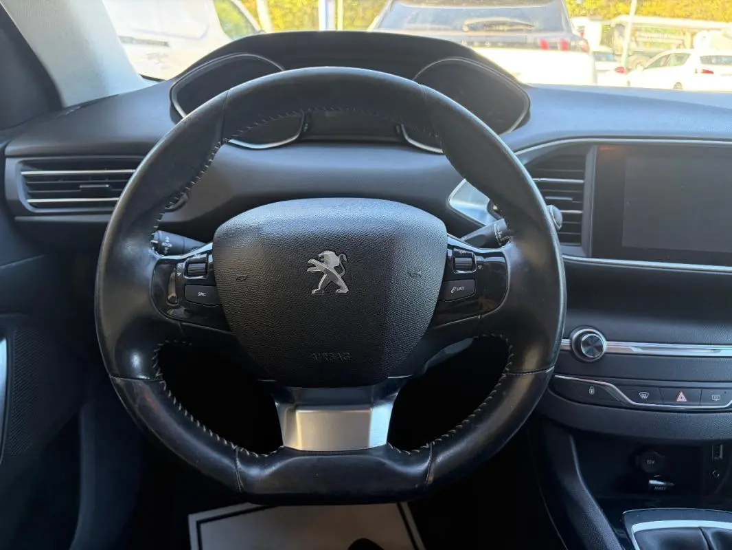 Vue rapprochée du volant noir de la Peugeot 308 Active 2014 avec tableau de bord et écran tactile en arrière-plan.