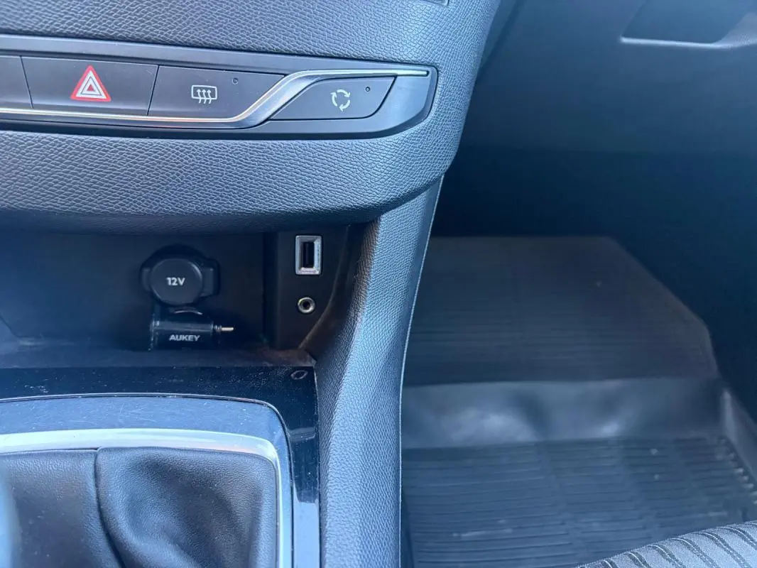 Gros plan sur la console centrale intérieure noire d'une Peugeot 308 Active 2014, avec prise 12V, port USB et commande de climatisation.