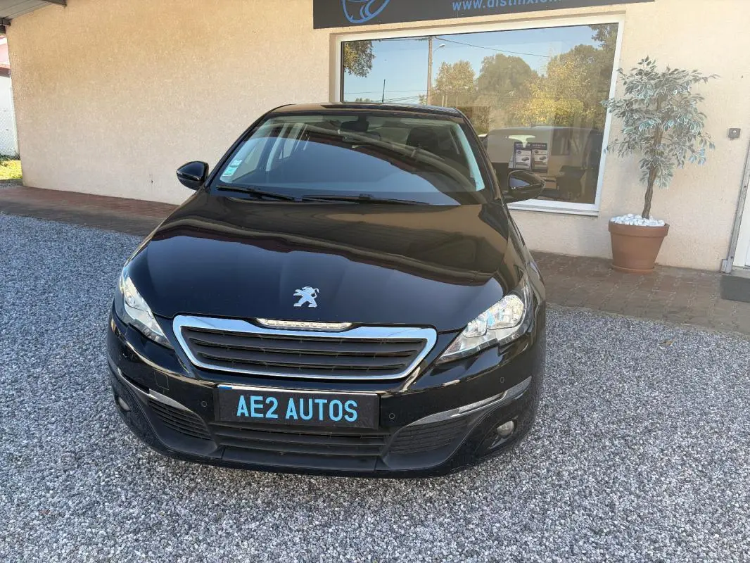 Peugeot 308 Active noire vue de face, avec calandre chromée et plaque AE2 AUTOS visible.