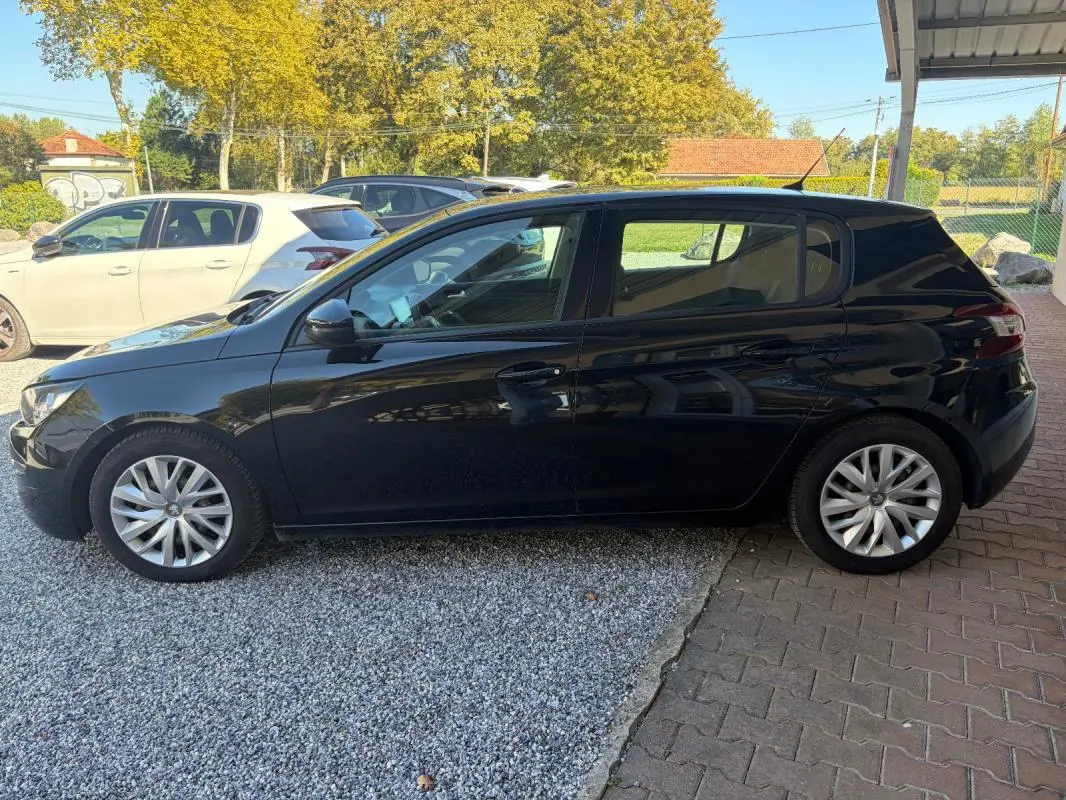 Peugeot 308 Active noire vue de profil côté gauche, garée sur sol mixte gravier et pavés sous abri.