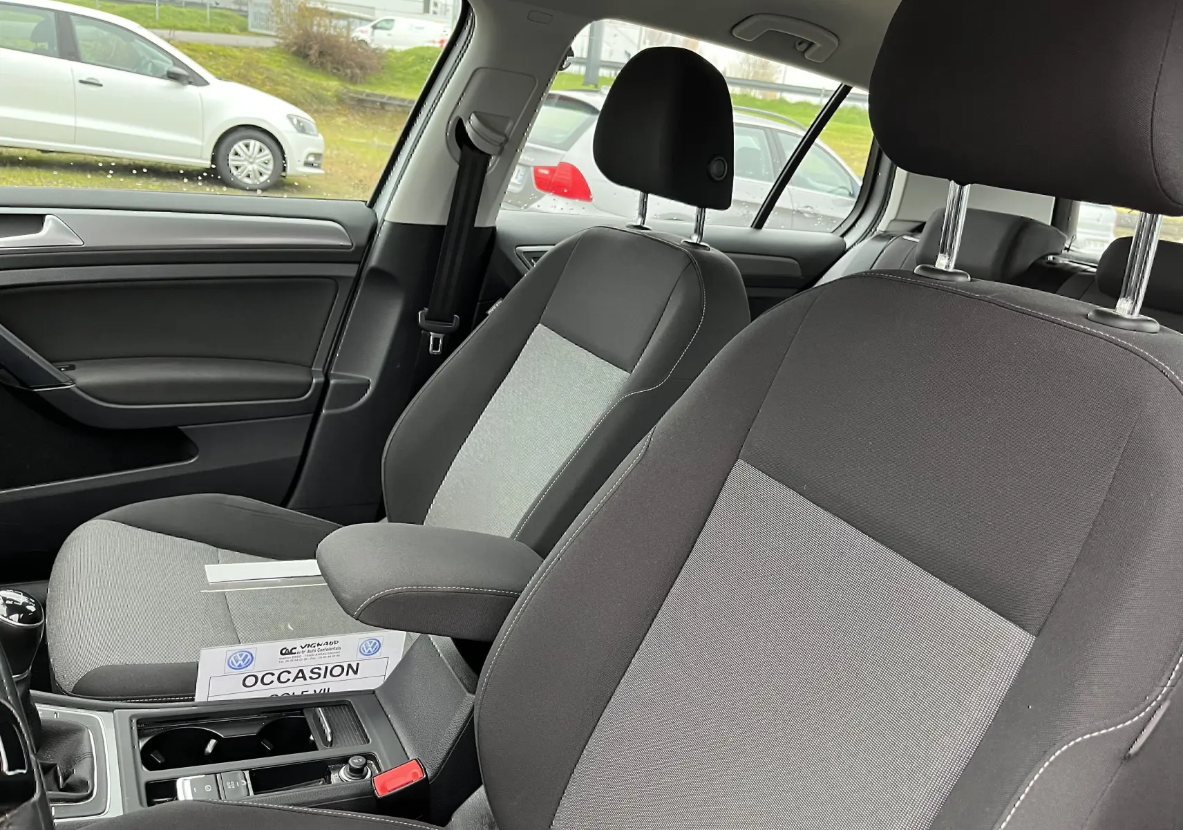 Intérieur de la Volkswagen Golf 7 2017 en tissu noir et gris, vue côté conducteur avec accoudoir central et levier de vitesse manuel.