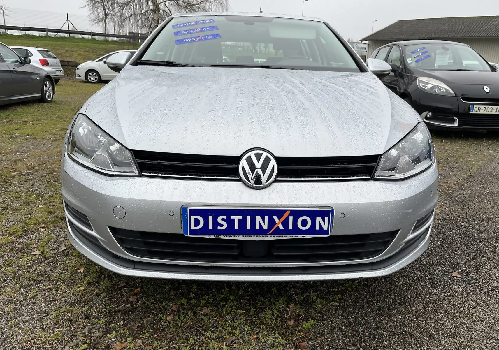 Vue frontale d'une Volkswagen Golf 7 argentée avec plaques Distinxion et gouttes de pluie visibles sur la carrosserie.