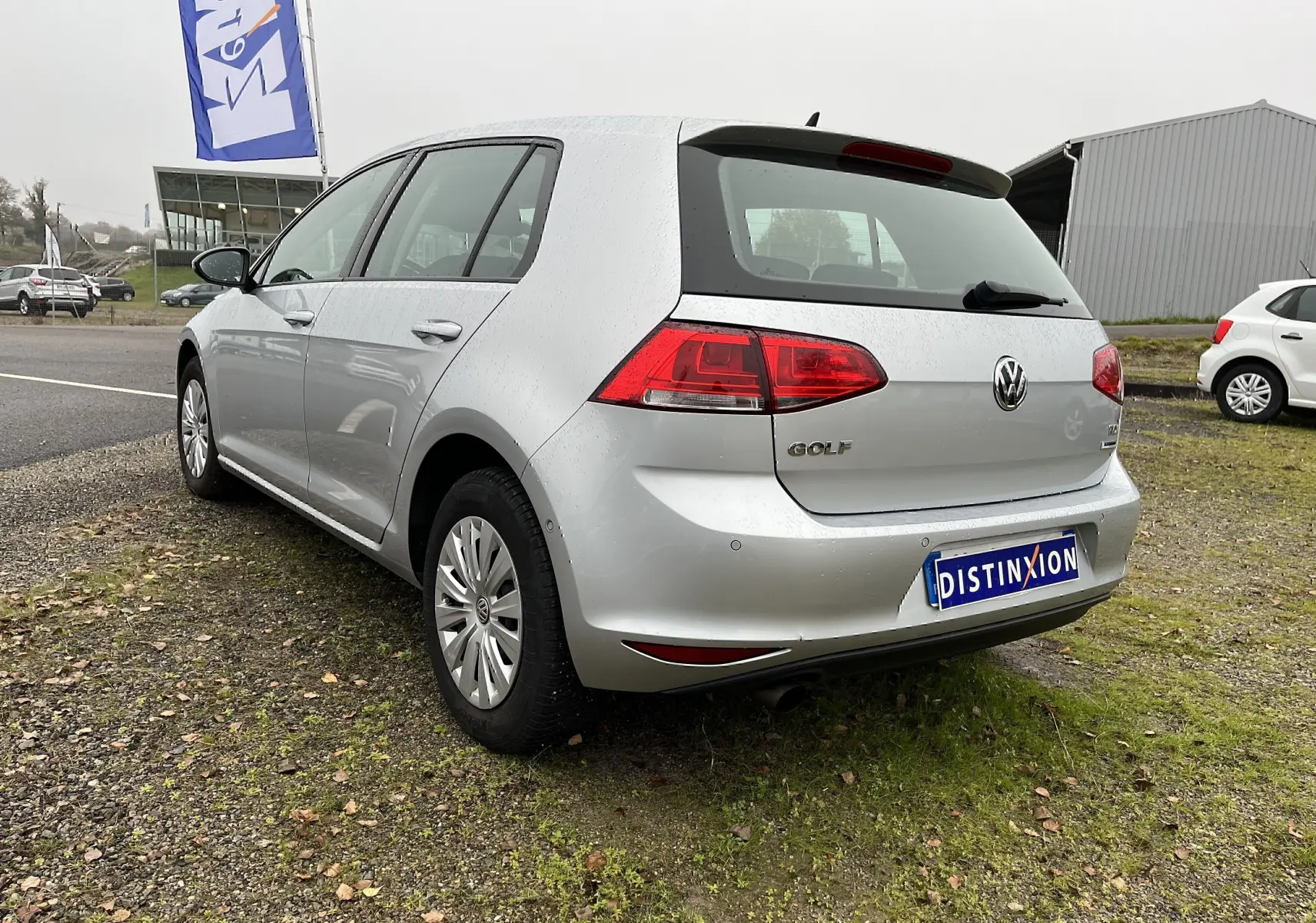 Volkswagen Golf 7 argent vue 3/4 arrière droit sur pelouse avec plaque Distinxion visible.