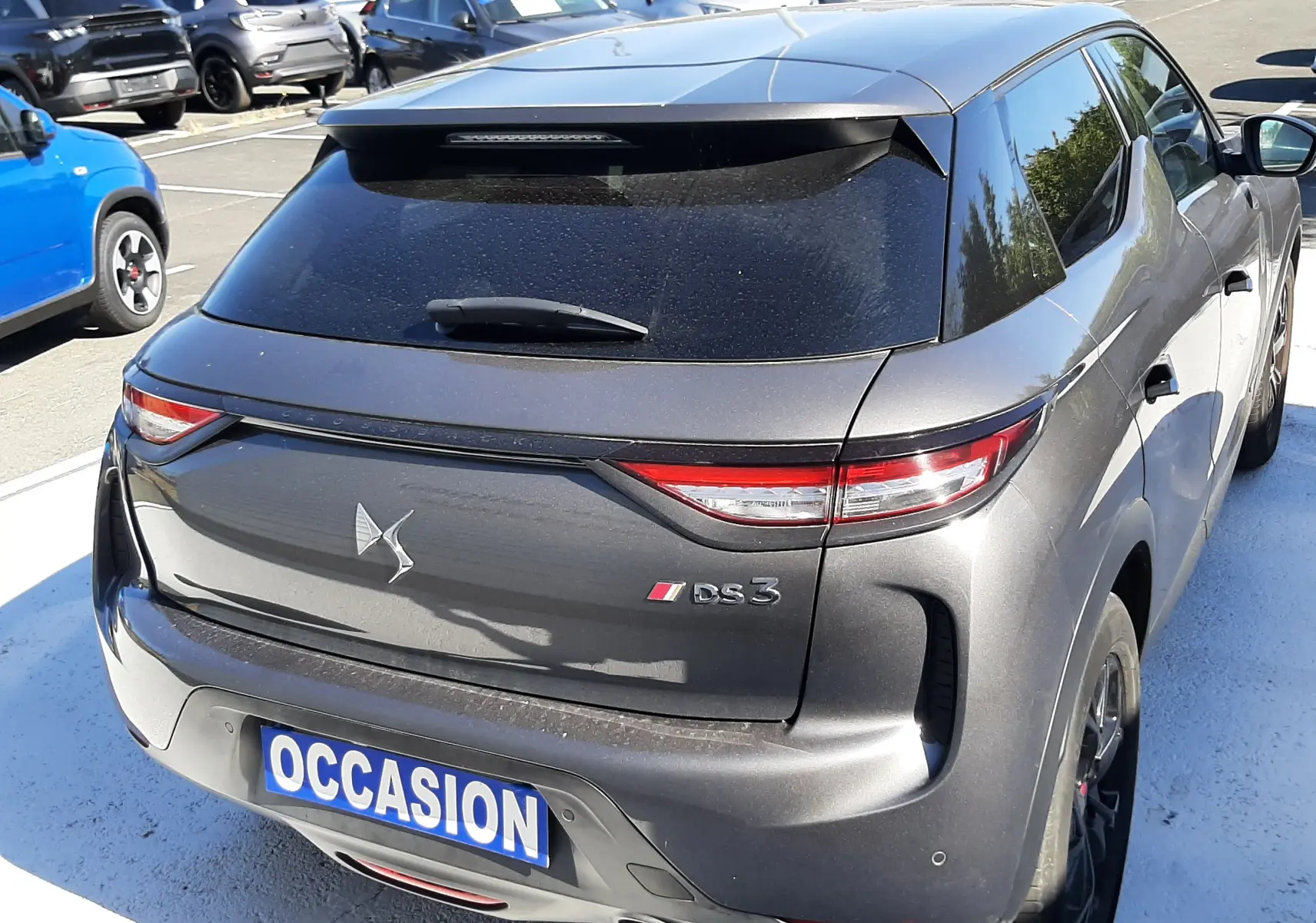 Vue 3/4 arrière d'un DS3 Crossback gris foncé avec feux LED et plaque "OCCASION" sur un parking extérieur.