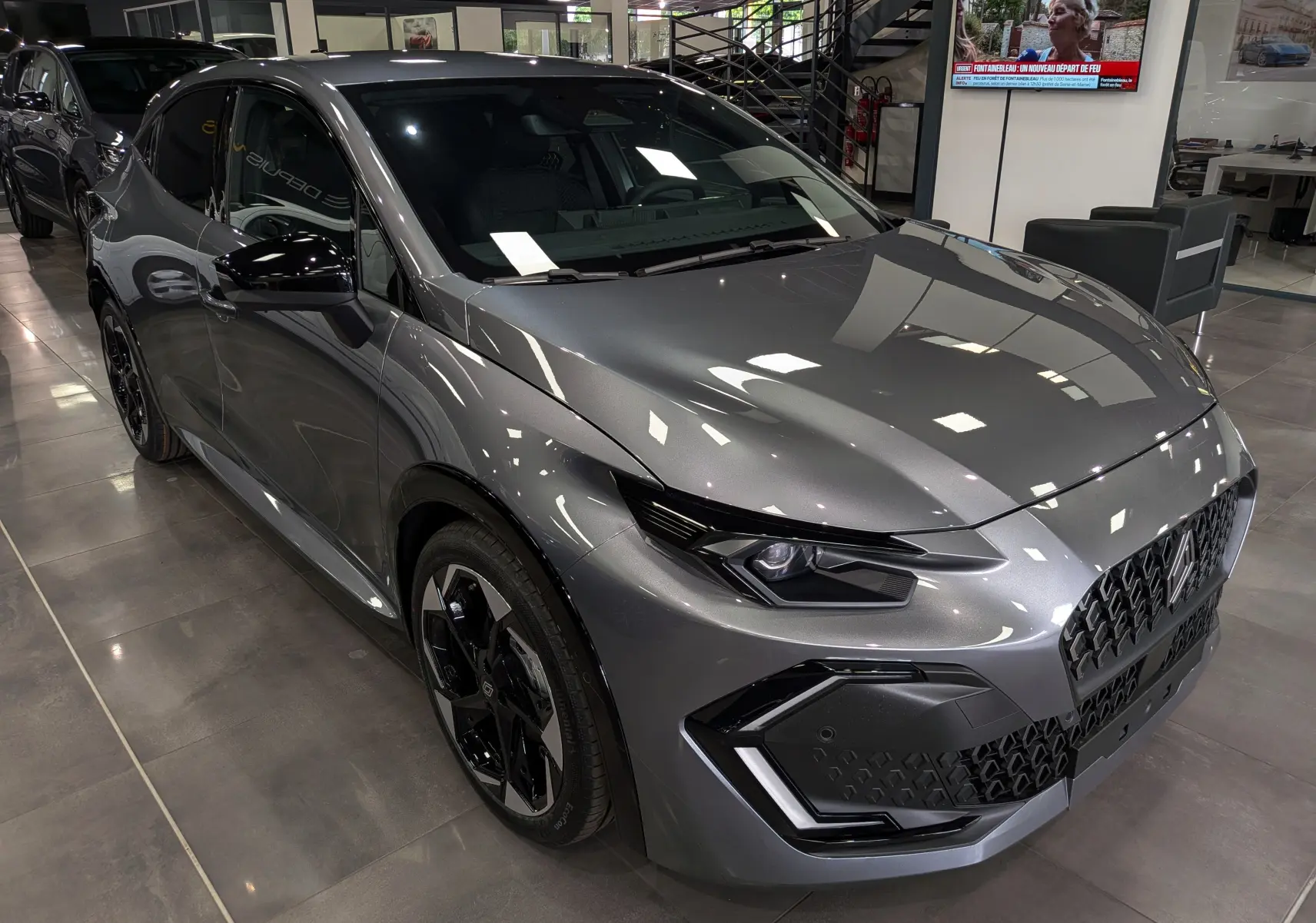 Renault Clio VI TCe 115 gris schiste vue 3/4 avant droit en intérieur, avec jantes noires et calandre distinctive.
