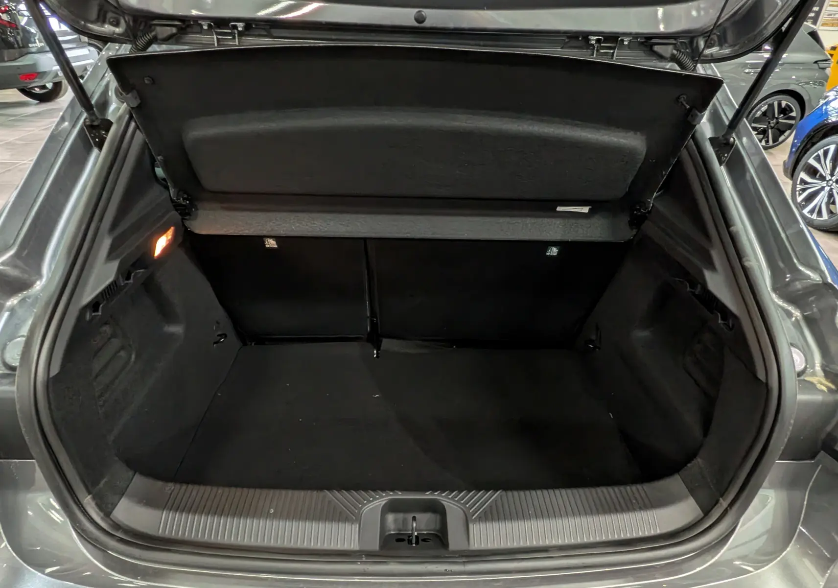 Vue arrière du coffre ouvert de la Renault Clio VI TCe 115 CH TECHNO gris schiste, montrant un espace de rangement vide et propre.