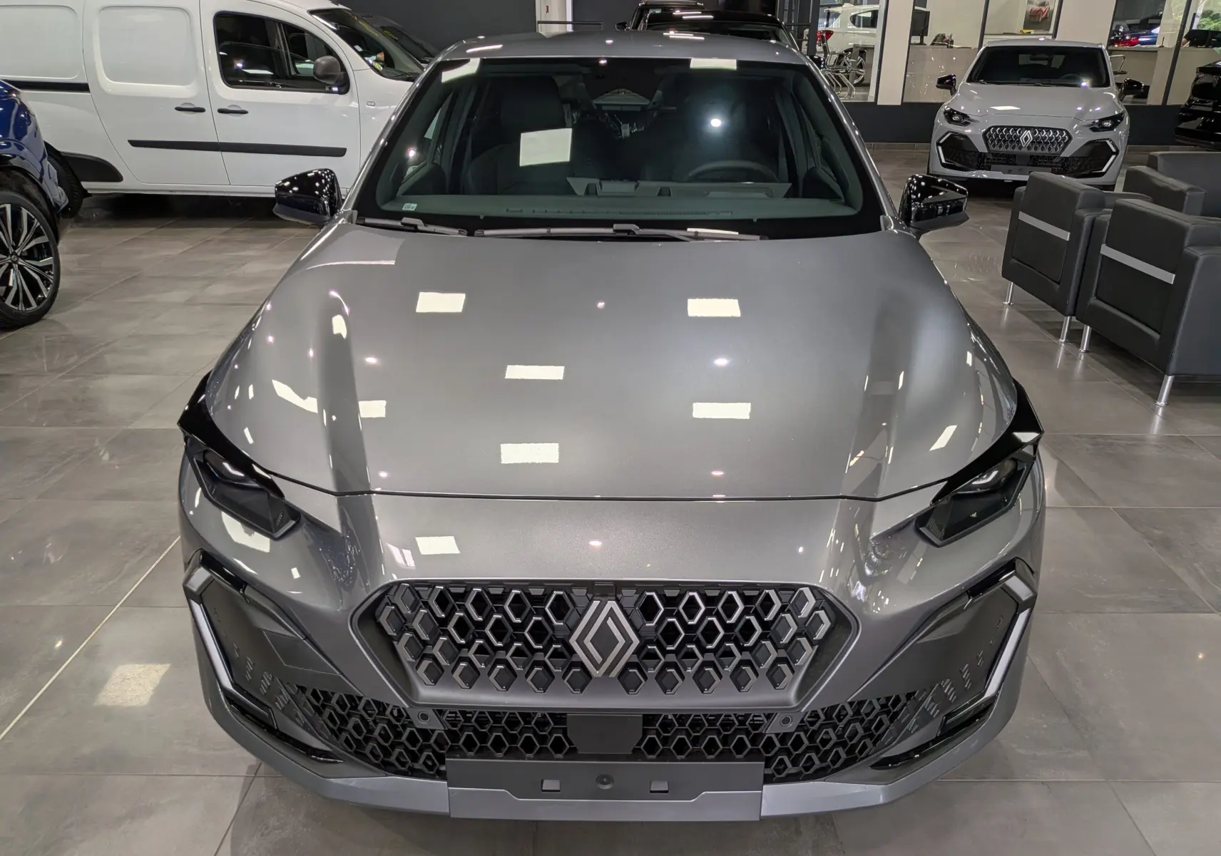 Vue frontale d'une Renault Clio VI TCe 115 CH TECHNO gris schiste, avec calandre hexagonale et phares LED marqués.