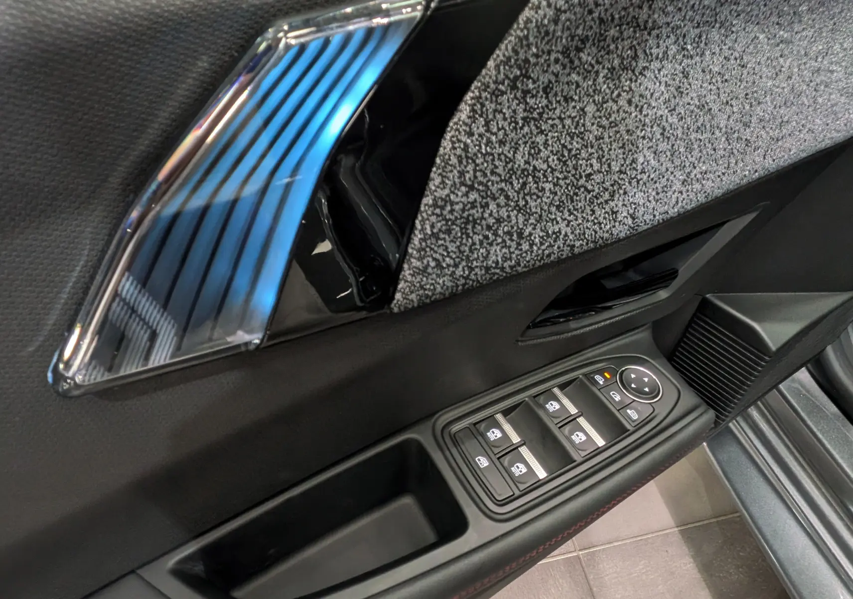 Détail de la porte côté conducteur de la Renault Clio VI TCe 115 gris schiste, avec commandes des vitres et insert décoratif chromé.