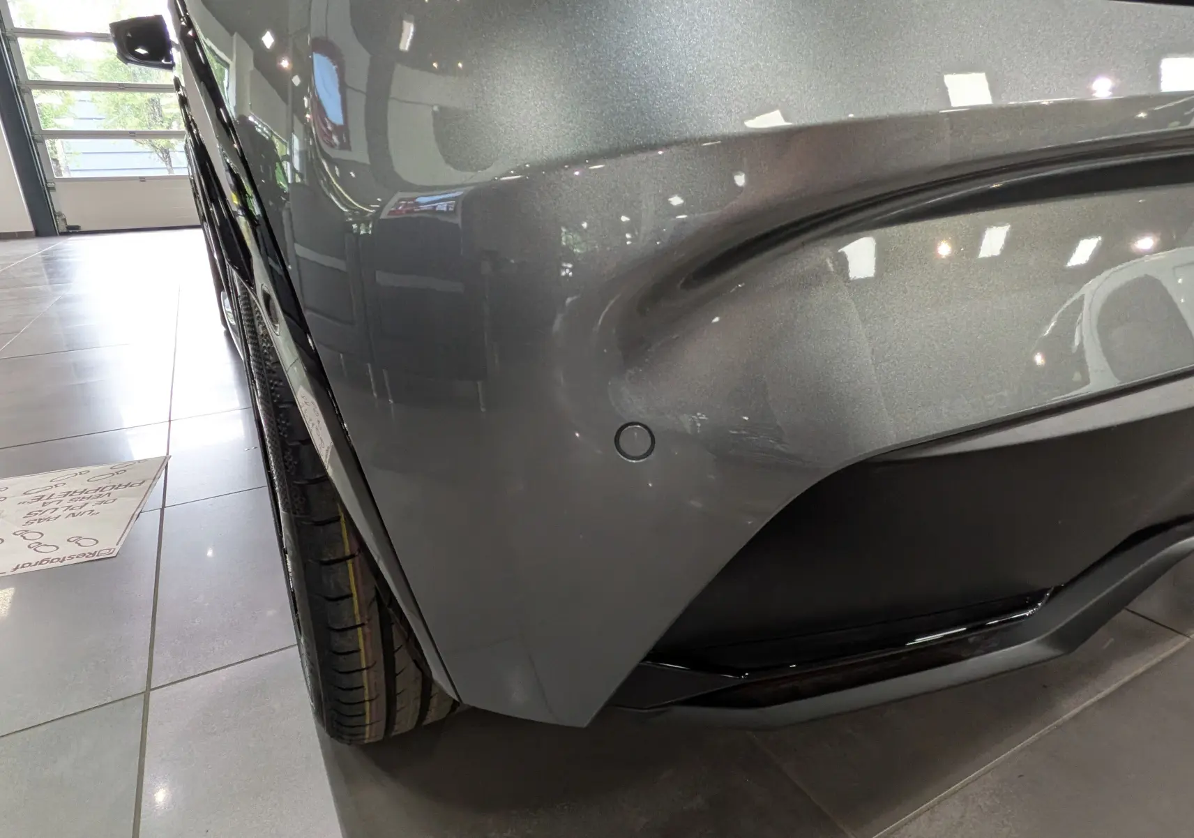 Gros plan sur l'angle avant droit gris schiste d'une Renault Clio VI TCe 115 CH TECHNO, avec capteur de stationnement visible.
