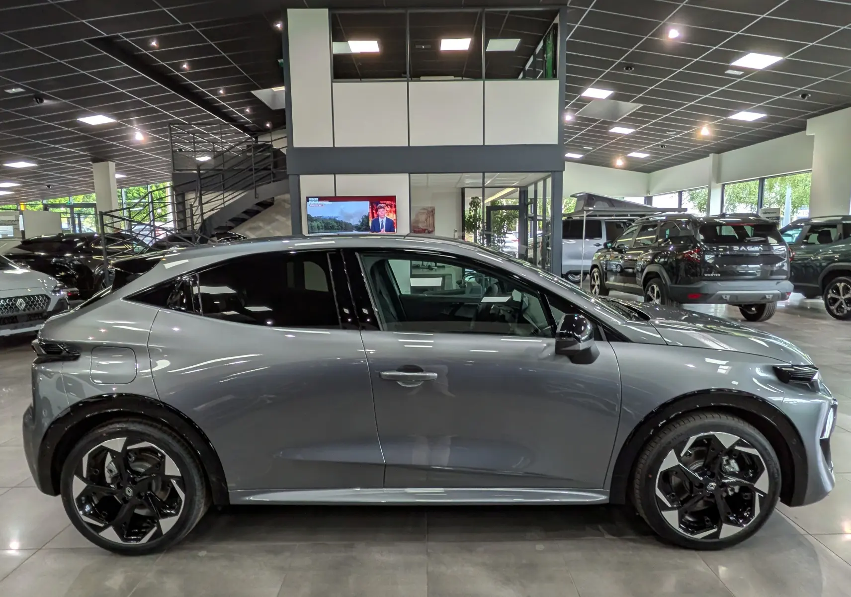 Profil droit d'une Renault Clio VI TCe 115 CH TECHNO gris schiste avec jantes bi-ton et vitres teintées en showroom.
