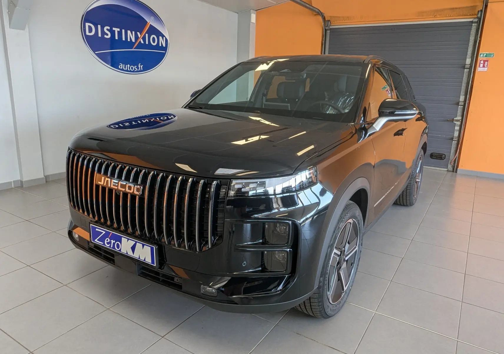 Vue 3/4 avant du SUV JAECOO J7 noir carbone métal avec calandre verticale et jantes modernes, en intérieur showroom.