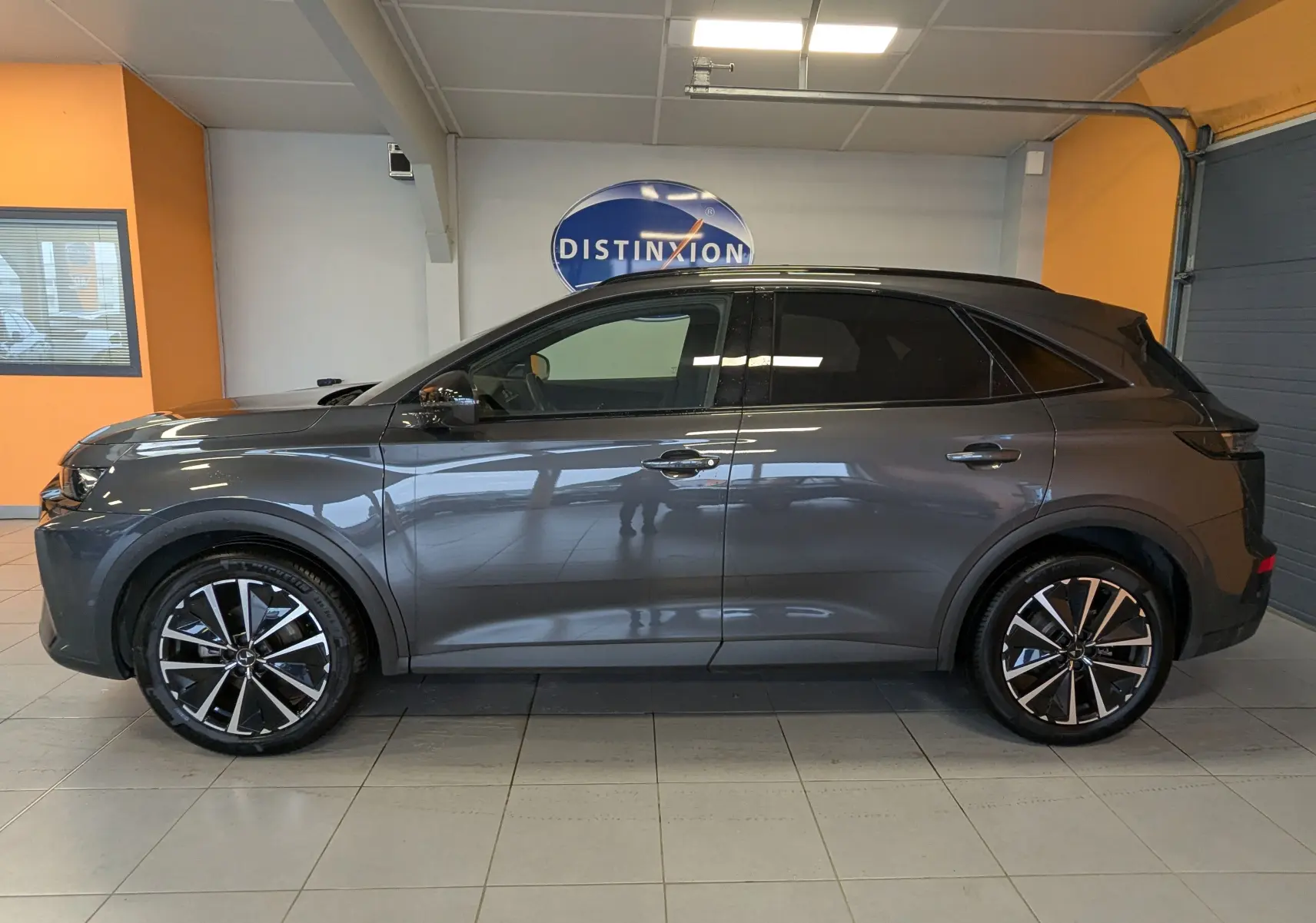 Vue de profil côté gauche d'un DS7 gris laqué avec jantes alliage 19 pouces bicolores dans un showroom.