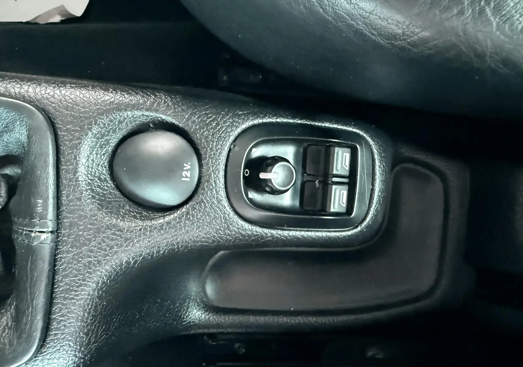 Gros plan sur la console centrale noire d’une Peugeot 206, montrant les commandes de vitres électriques et prise 12V.