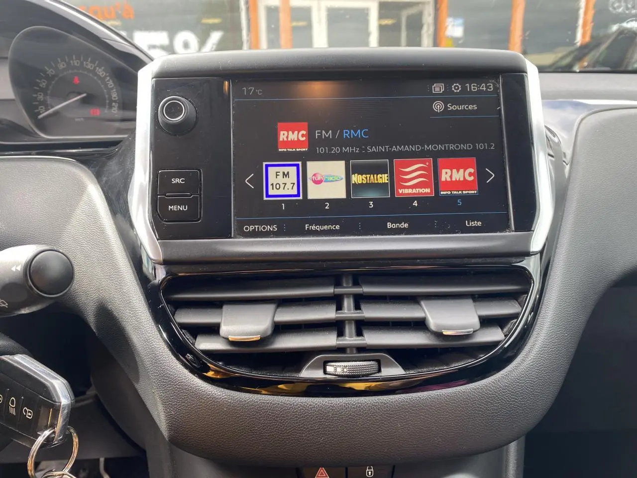 Tableau de bord de Peugeot 208 gris 2018 avec écran tactile affichant les stations radio FM, vue frontale rapprochée.