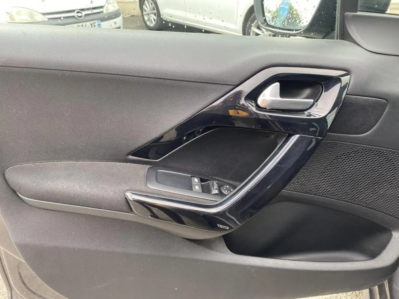 Gros plan sur la porte côté gauche de la Peugeot 208 gris, montrant la poignée et les commandes des vitres électriques.