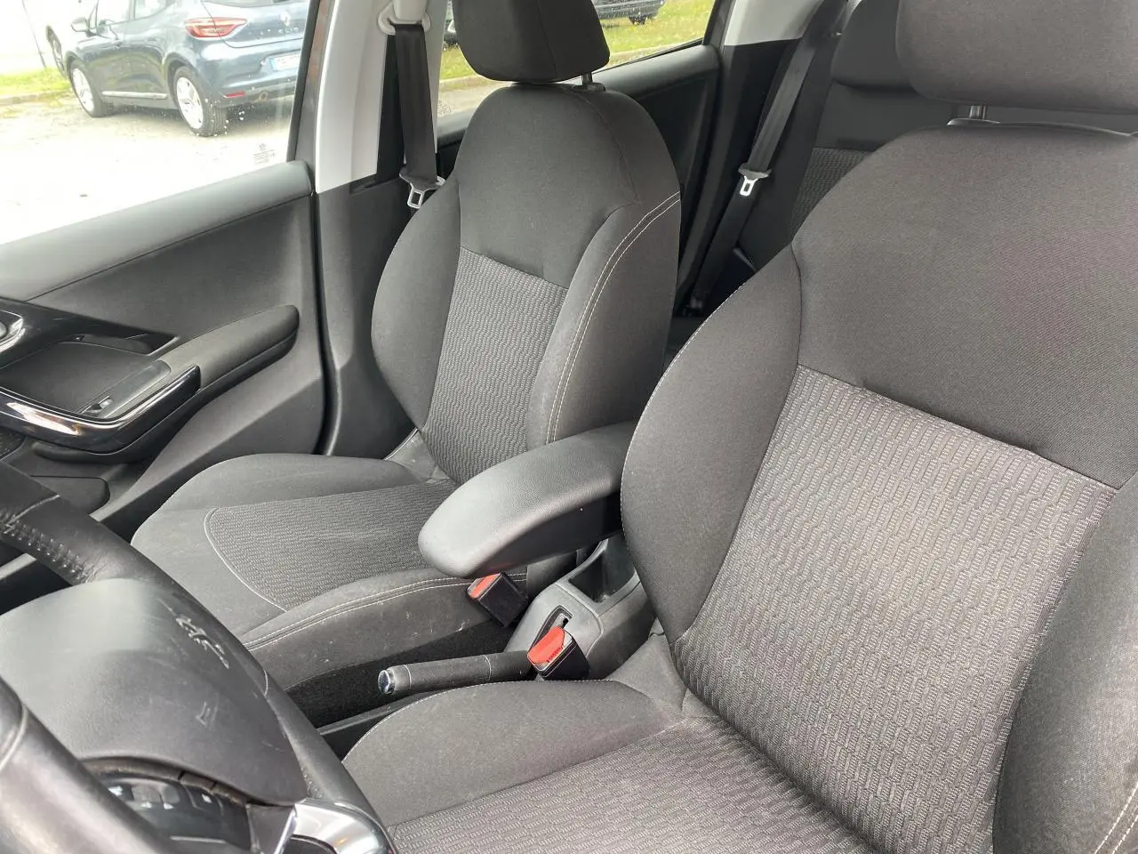 Vue intérieure rapprochée des sièges avant gris foncé de la Peugeot 208 avec accoudoir central et ceinture de sécurité.
