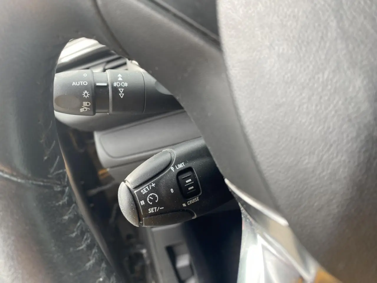 Gros plan sur le volant de la Peugeot 208 gris, montrant la commande du régulateur de vitesse et le commodo d'éclairage.
