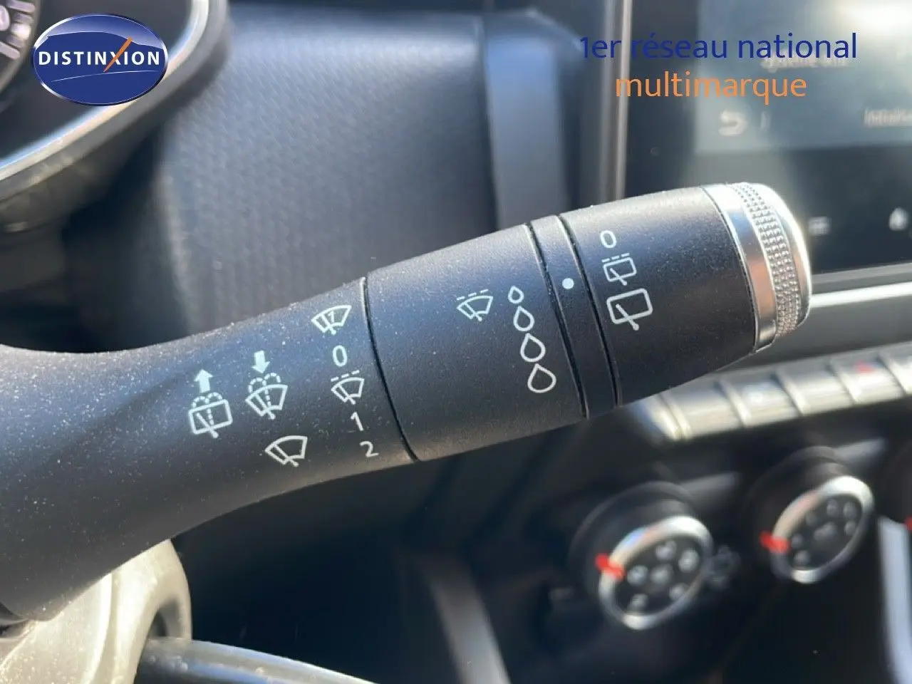 Gros plan sur la manette d'essuie-glace à gauche du volant d'une Renault Clio blanc glacier, tableau de bord en arrière-plan.