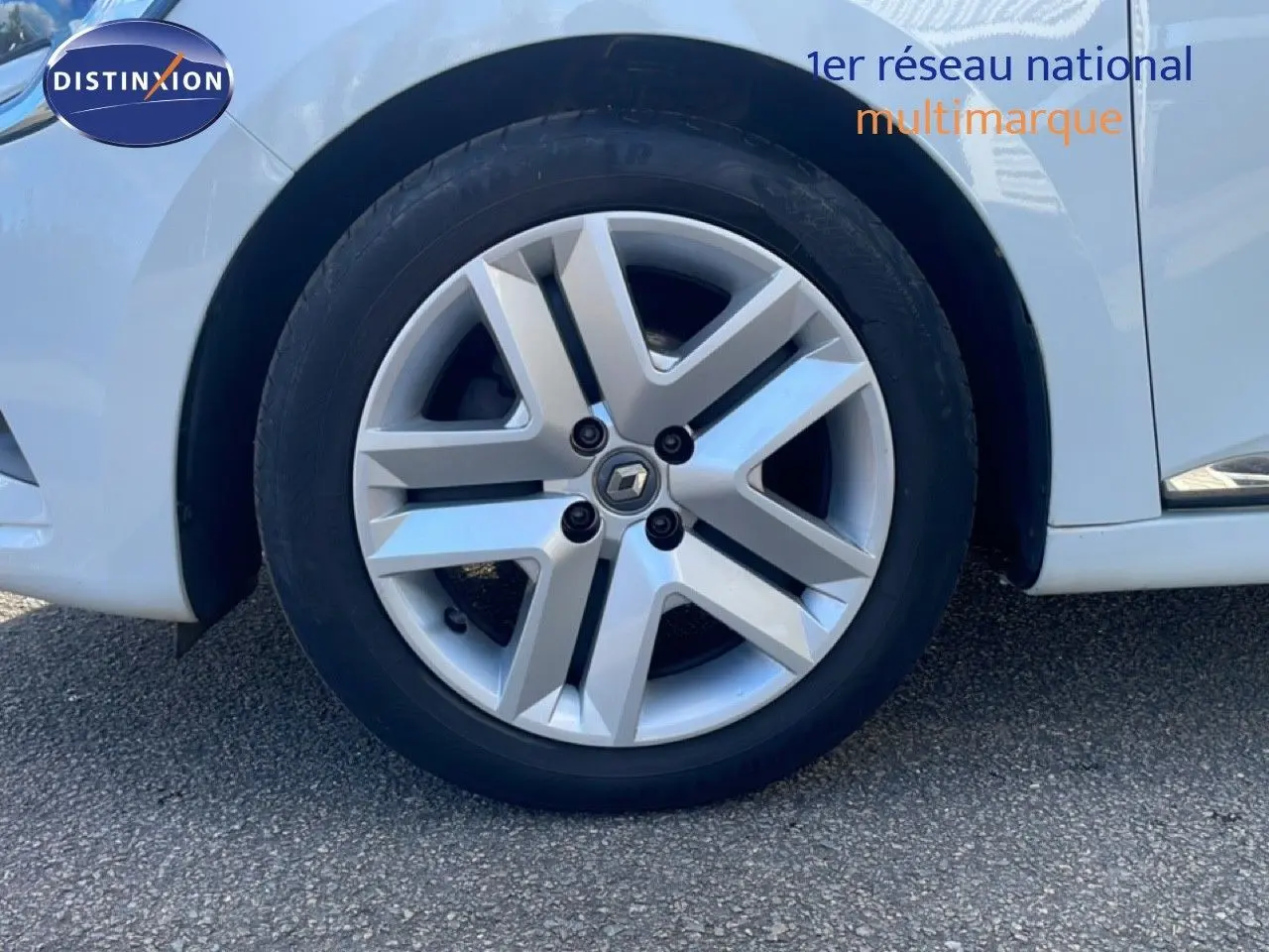 Gros plan sur la roue avant gauche d'une Renault Clio blanc glacier avec jante alliage au design moderne.