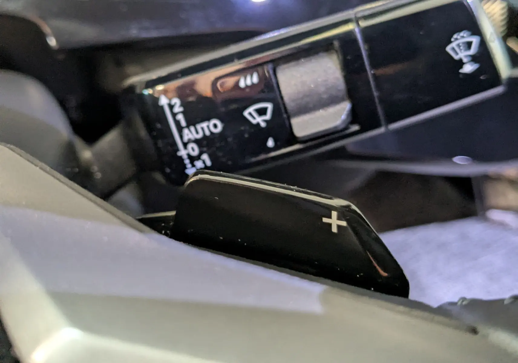Gros plan sur la palette de changement de vitesse "+" noire et le commodo de réglage des essuie-glaces dans l’habitacle du Peugeot 3008 noir.