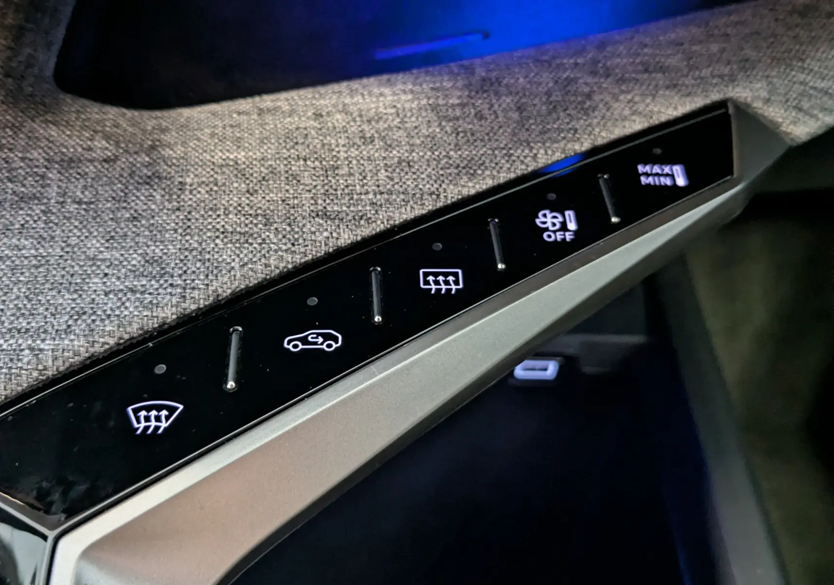 Gros plan sur les commandes tactiles noires de la console centrale, avec tissu gris texturé en arrière-plan dans un Peugeot 3008 noir.