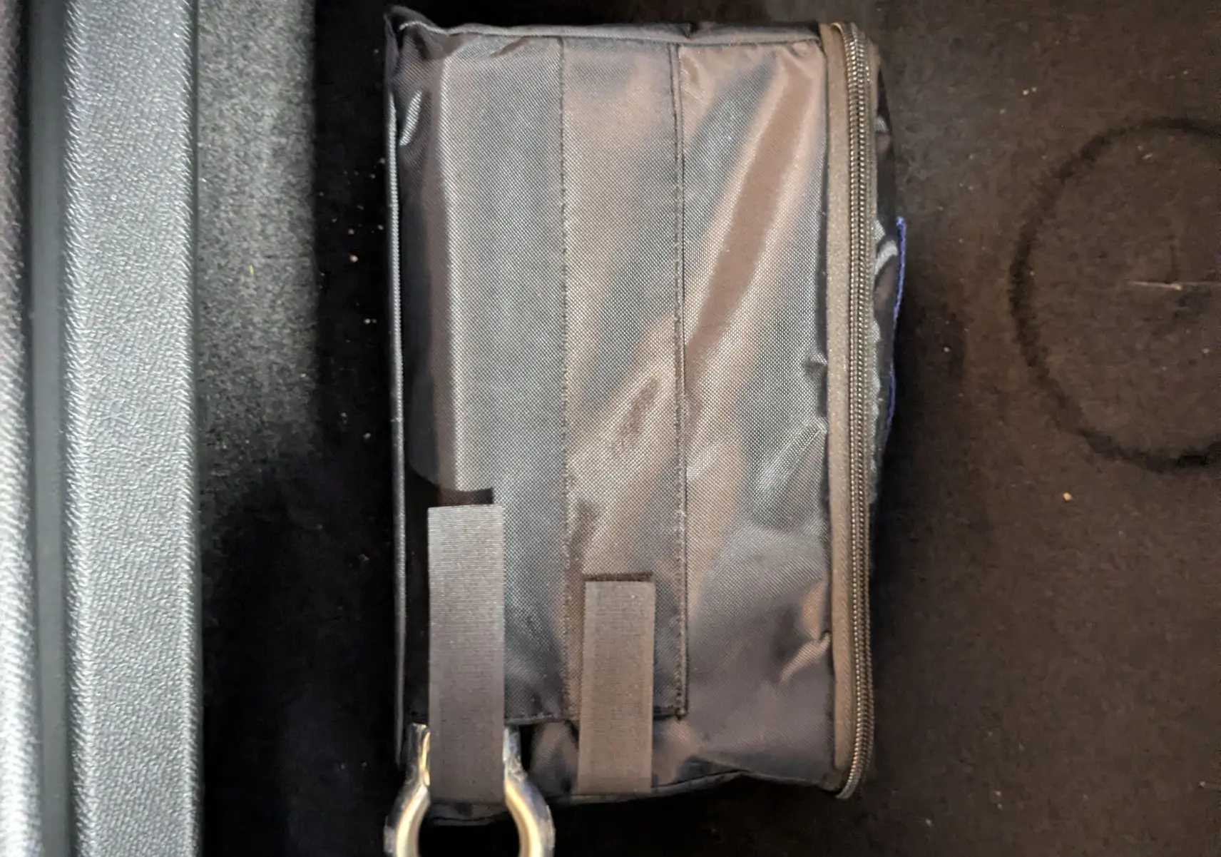 Gros plan sur un sac noir avec anneau métallique posé sur le tapis noir intérieur d’un Peugeot 3008 hybride.