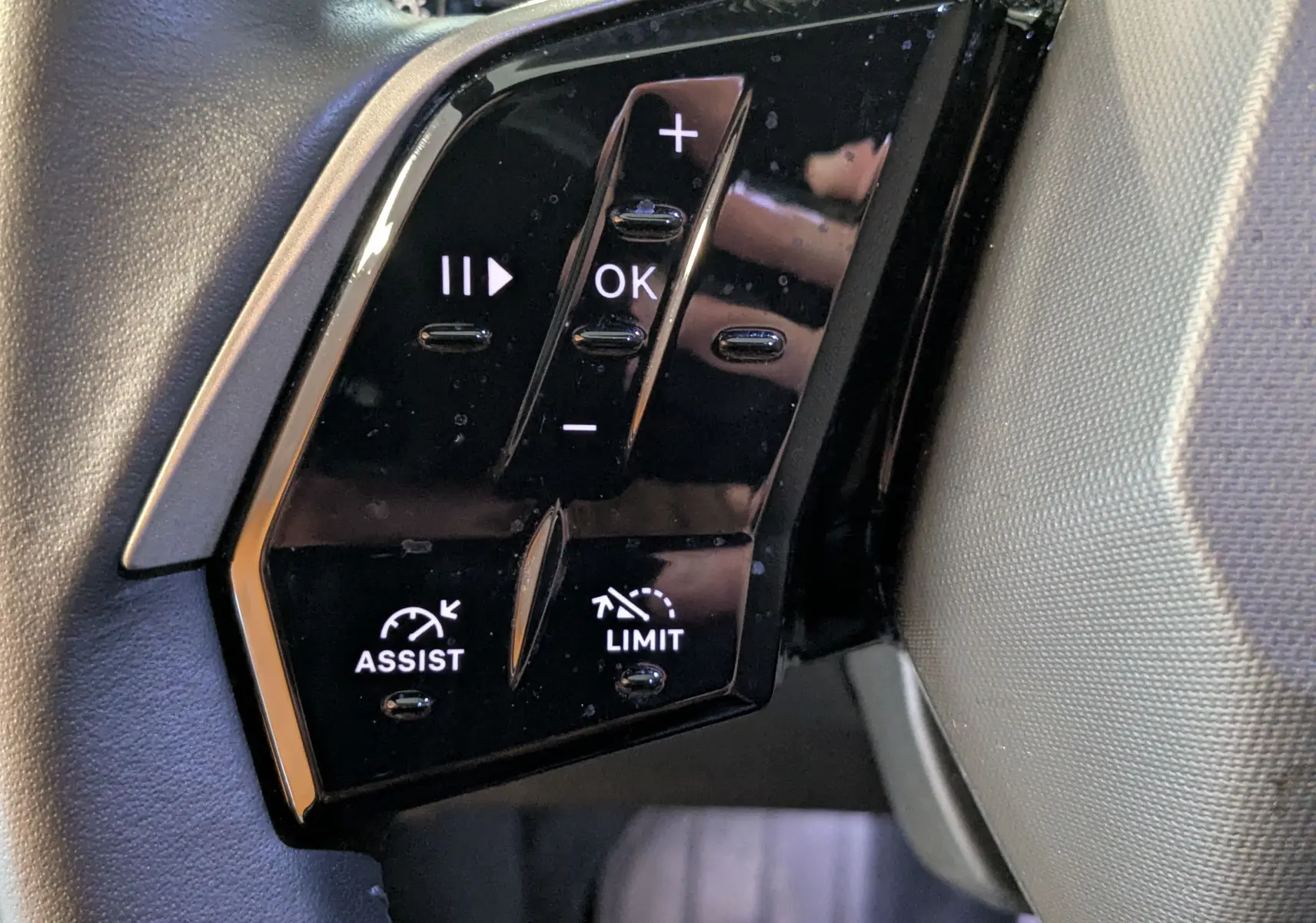 Gros plan sur les commandes noires du volant cuir du Peugeot 3008 Hybrid 145, avec boutons de régulateur et assistant.