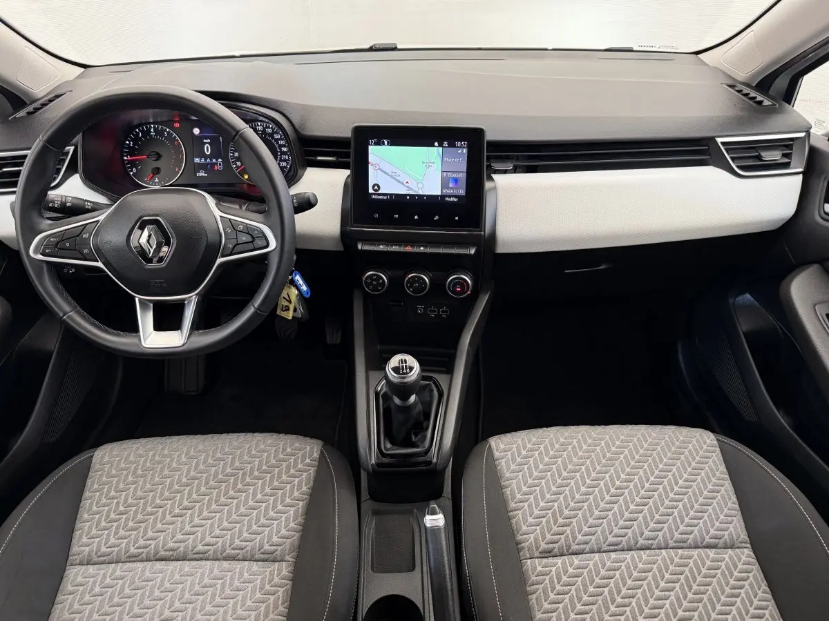 Vue intérieure avant de la Renault Clio 2023 Evolution TCe 100 GPL, tableau de bord clair avec écran tactile central et volant cuir.