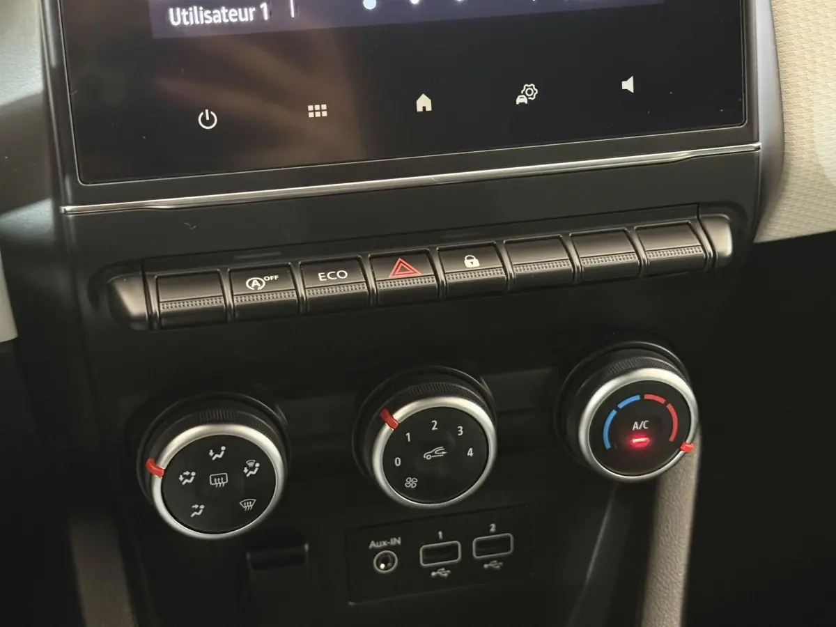 Gros plan sur les commandes de climatisation et boutons fonctionnels du tableau de bord central de la Renault Clio blanche Evolution TCe 100 GPL 2023.