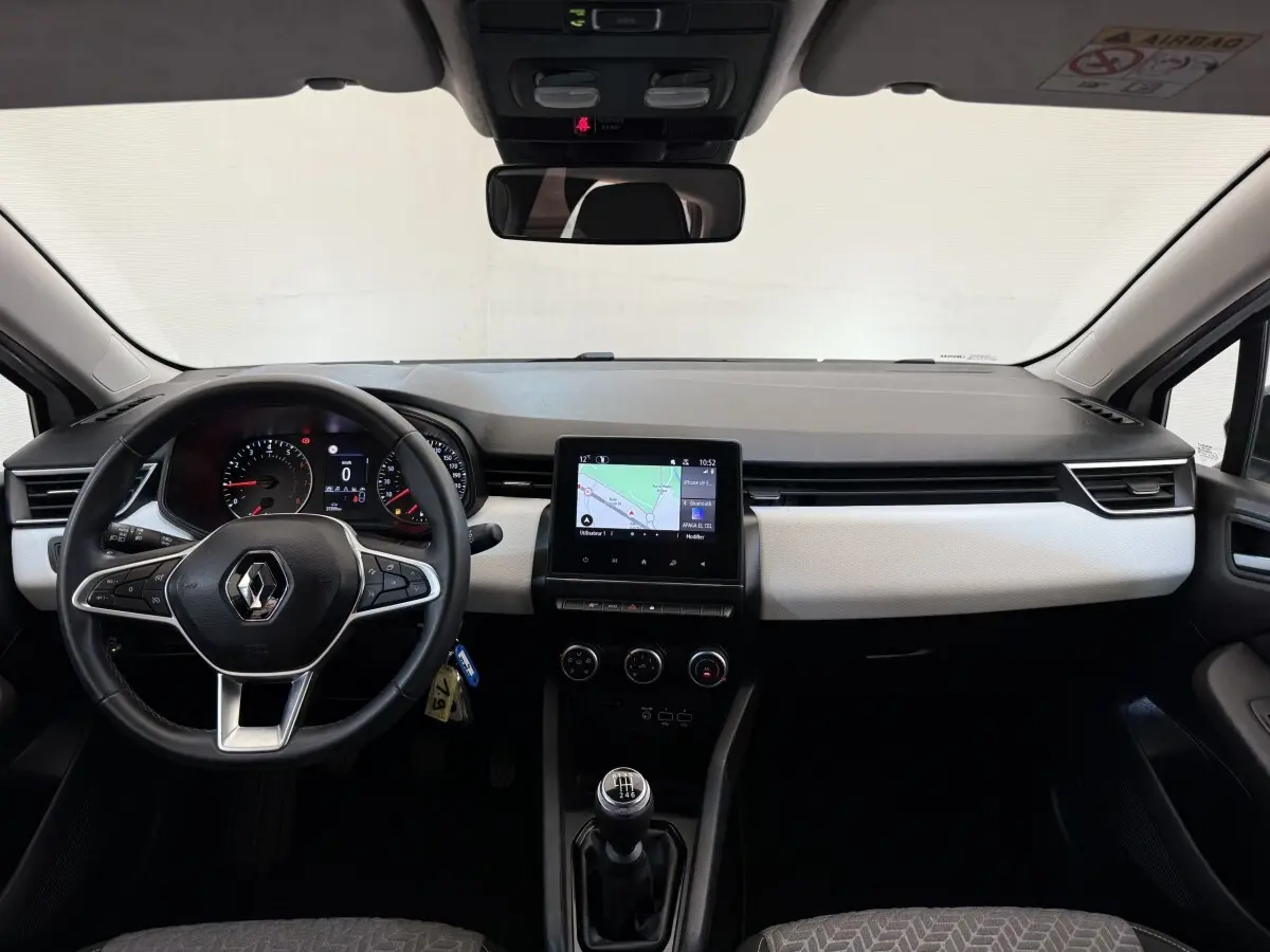 Vue frontale de l’habitacle de la Renault Clio blanche 2023, avec tableau de bord moderne et écran tactile central.