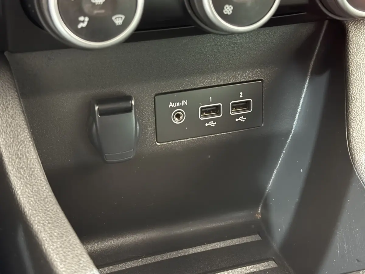 Gros plan sur la console centrale noire de la Renault Clio blanche, montrant les ports USB et prise Aux-IN.