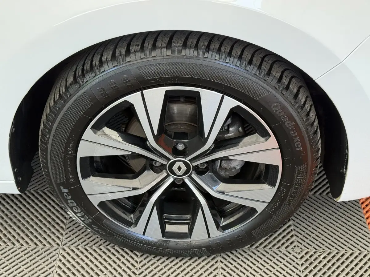 Gros plan sur la roue avant droite d’une Renault Clio blanche, avec jante alliage noire et argentée au design moderne.